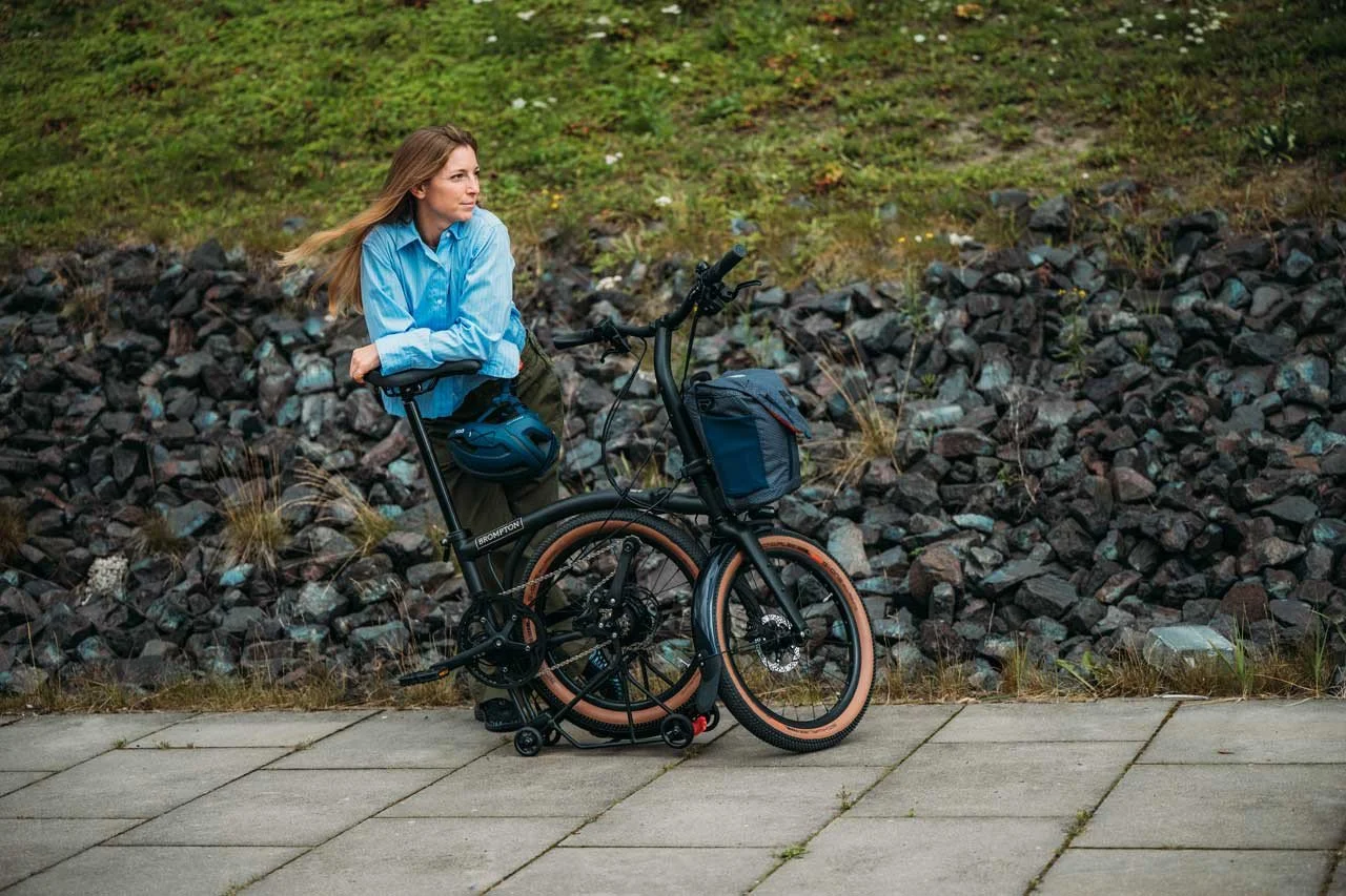 A person with half folded Brompton G line folding bike in country side setting.