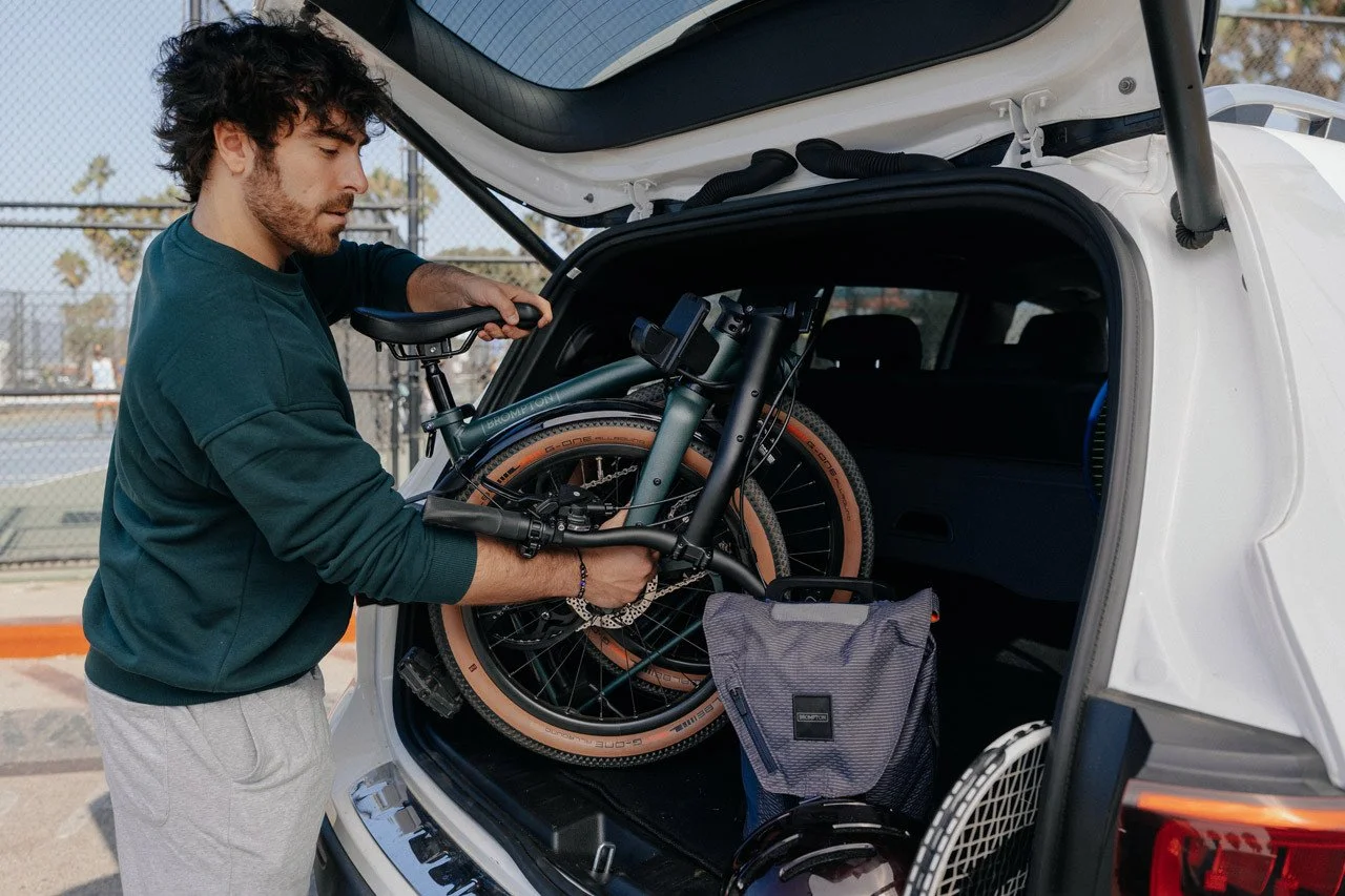A person loading a Brompton G Line Folding bike at the back of a white car.