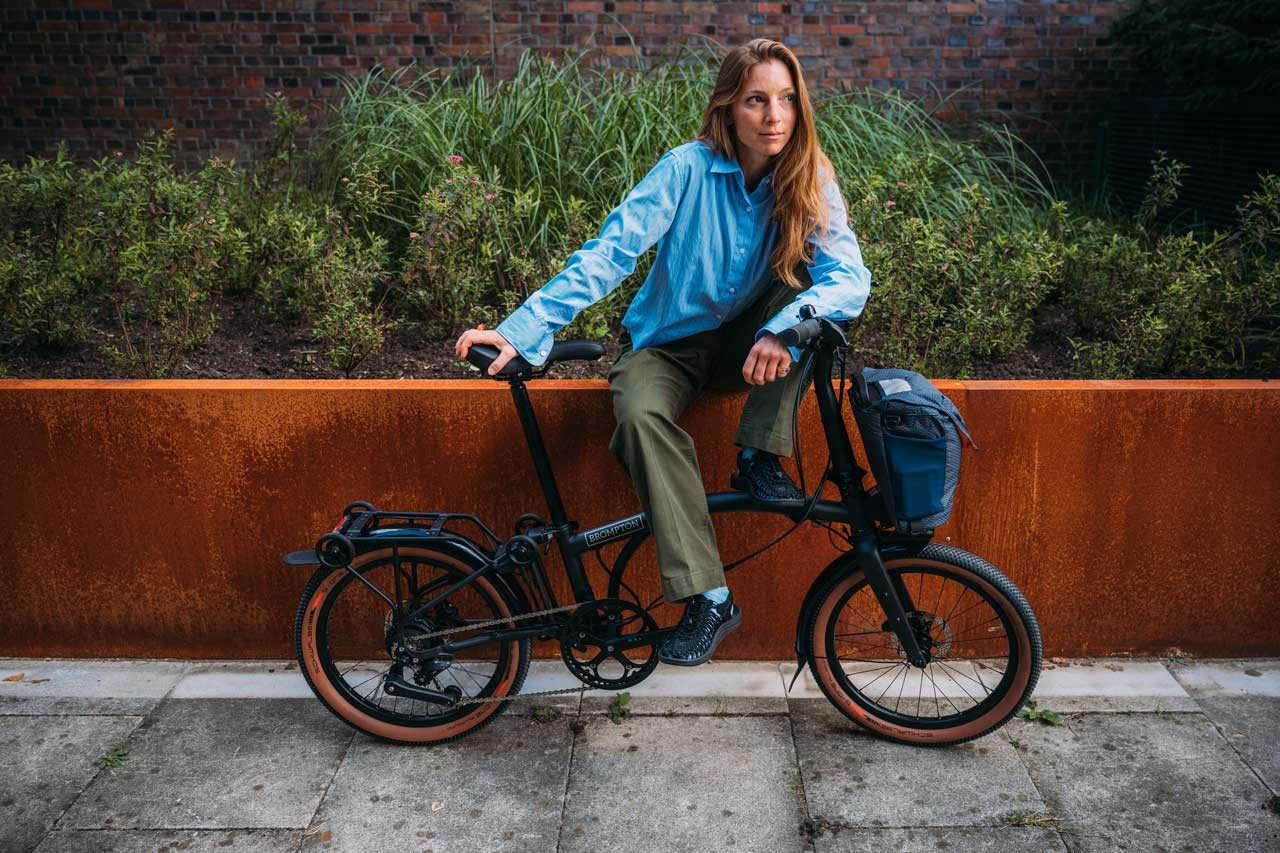 A person sitting on the wall with black Brompton G line folding bike.