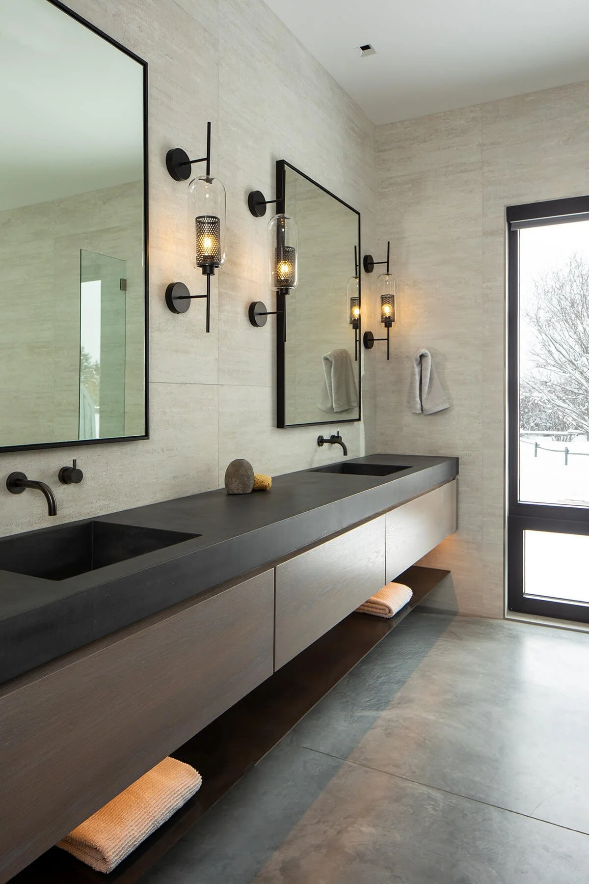 Dark grey double concrete vanity in bathroom in a modern home in Jackson Hole with a window looking out at a snowy landscape.