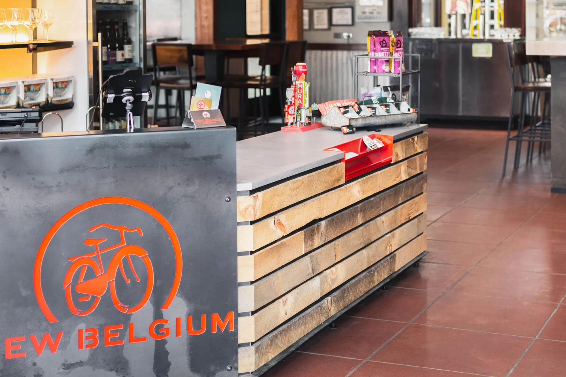 Merchandising check out counter at New Belgium tasting room featuring grey concrete countertops, metal signage and retail displays.
