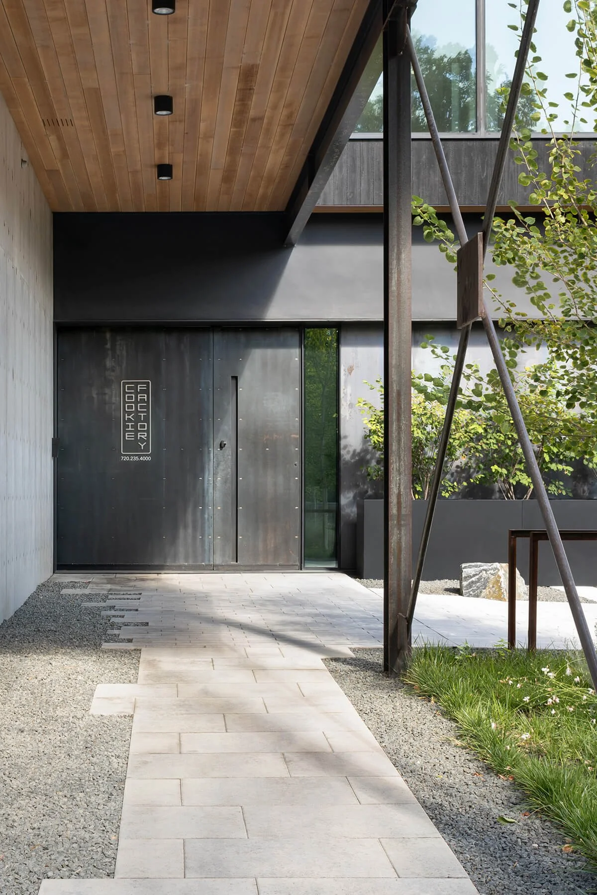 Entry to a renovated historic industrial building featuring a custom steel door, exterior metal cladding, and exposed structural steel with a minimal landscape approach