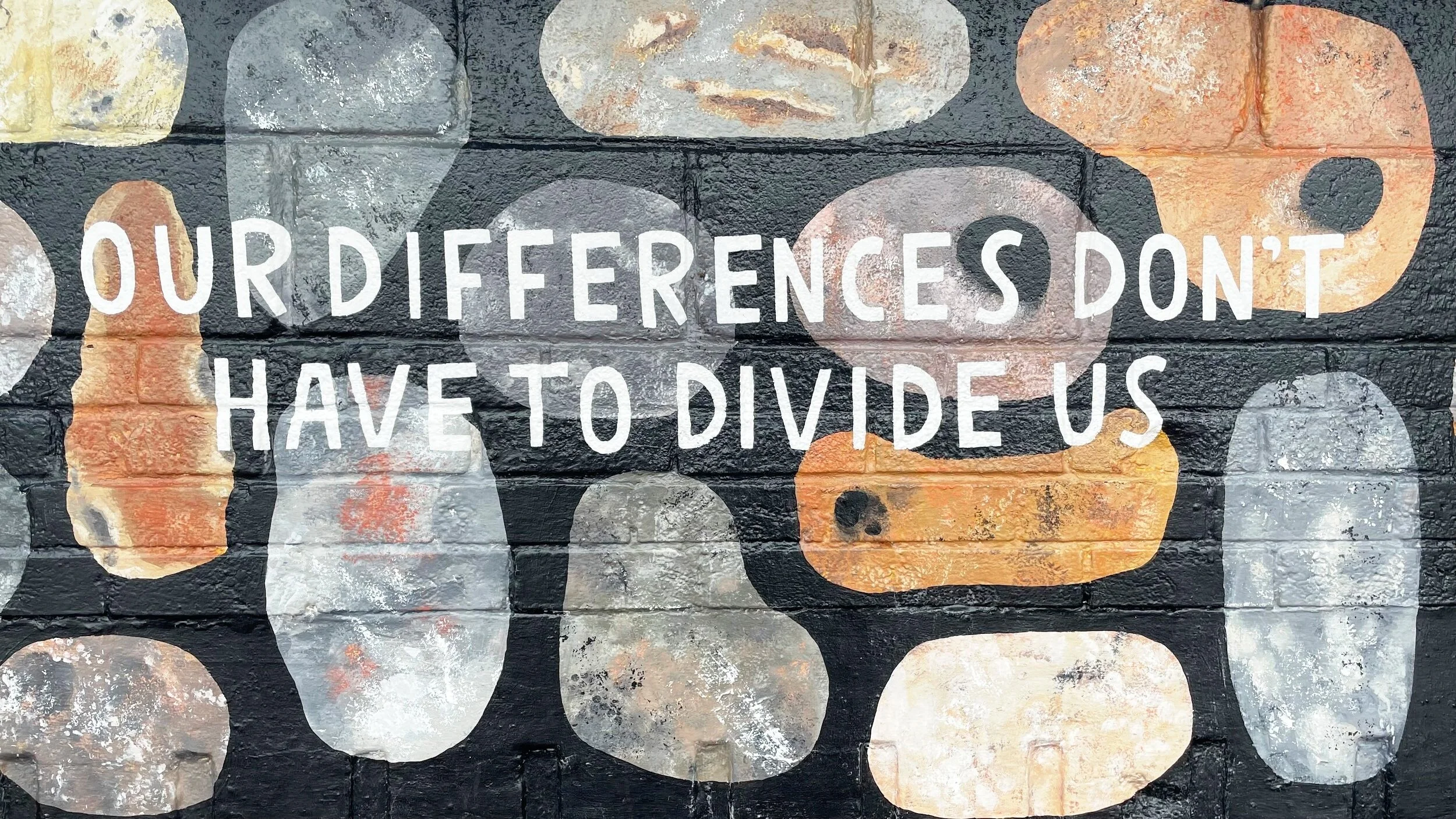 Graffiti art on a brick wall with abstract shapes and colors, with white text that reads 'Our differences don't have to divide us'.