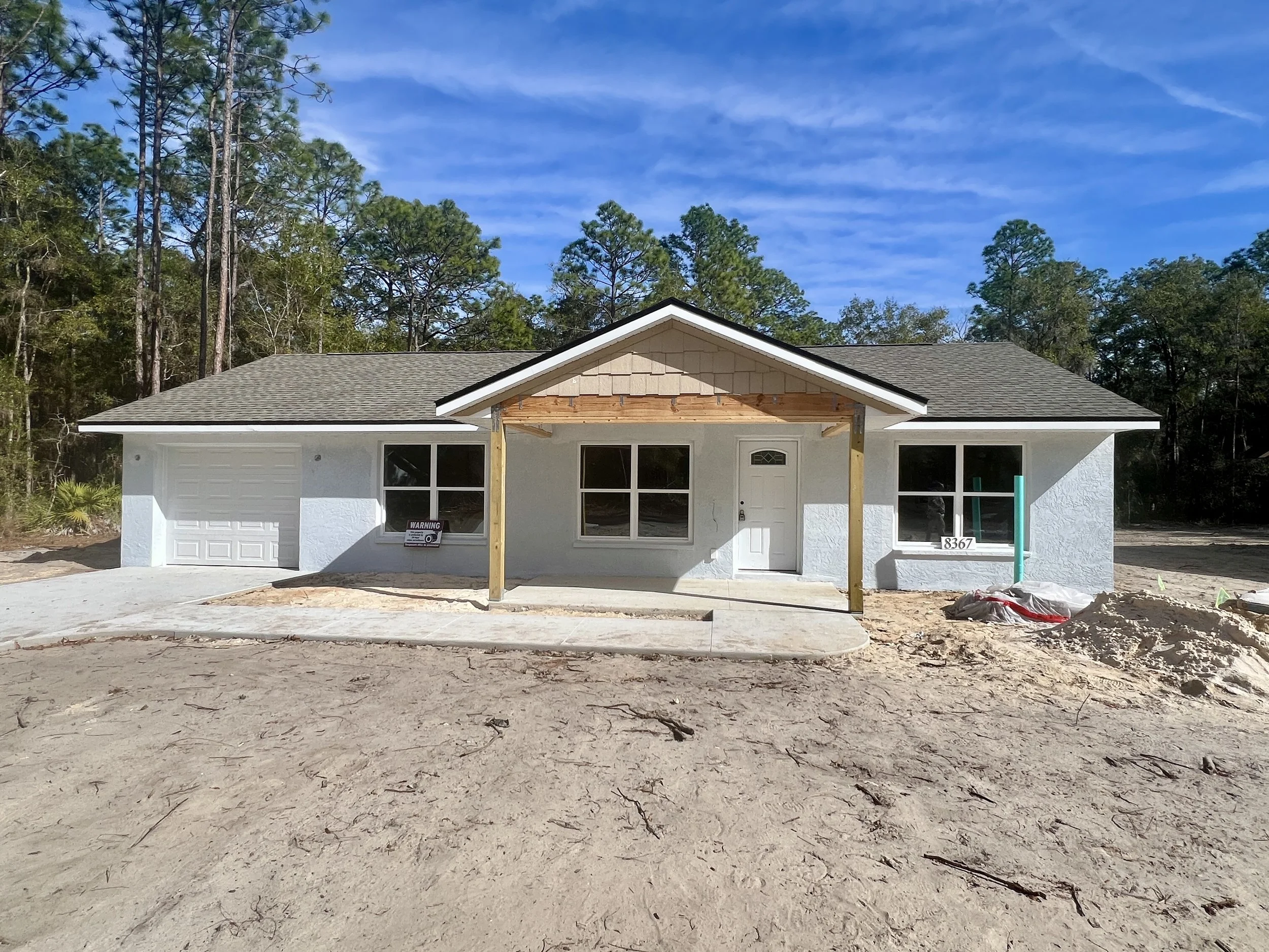 Exterior of an unpainted single story home currently under construction with grey asphalt shingled roof and sitting on a dirt lot without grass yet 