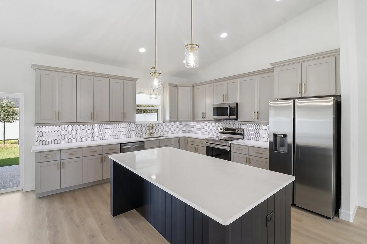 Modern kitchen with white cabinets, black and stainless steel appliances, a large island with a white countertop, pendant Lighting, and a honeycomb tile backsplash.