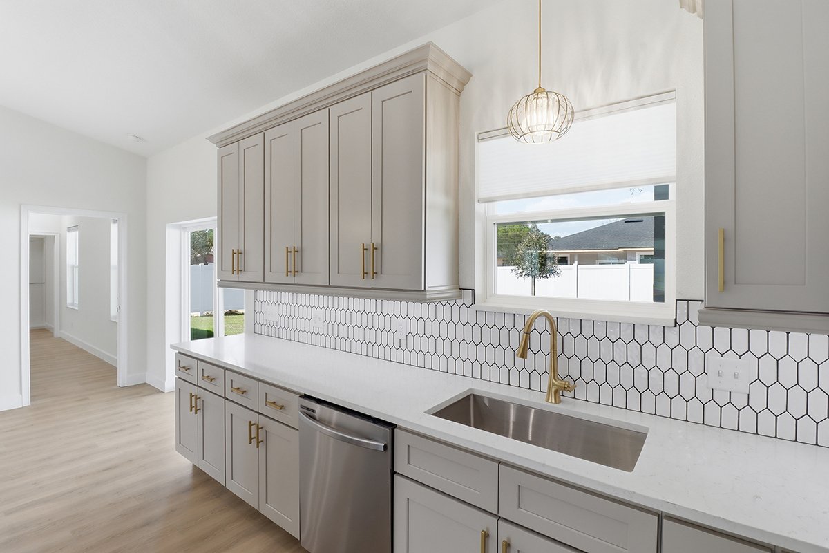 Modern kitchen with white cabinets, a marble countertop, a stainless steel sink with a gold faucet, black and white honeycomb tile backsplash, a window with a white screen, and a hanging light fixture.