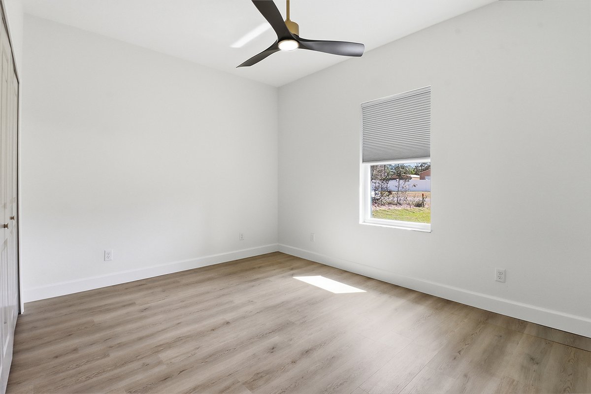 Empty room with white walls, a window with a blind, and a ceiling fan, with light-colored wood flooring and baseboards.