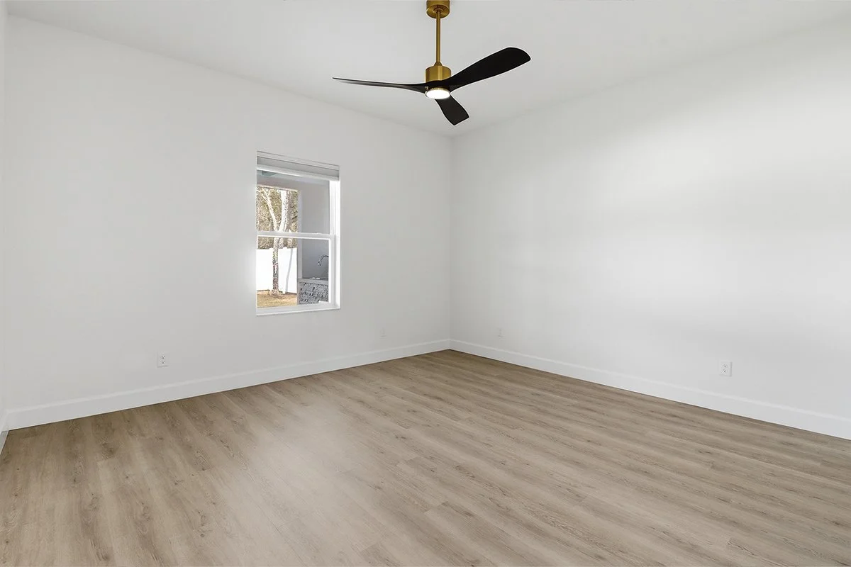 Empty room with white walls, a ceiling fan, and wood laminate flooring, with a window showing trees outside.
