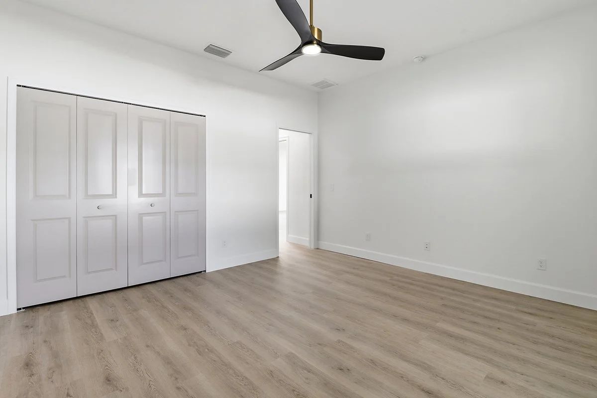 Empty bedroom with white walls, a ceiling fan, a closet with sliding doors, and light wood flooring.