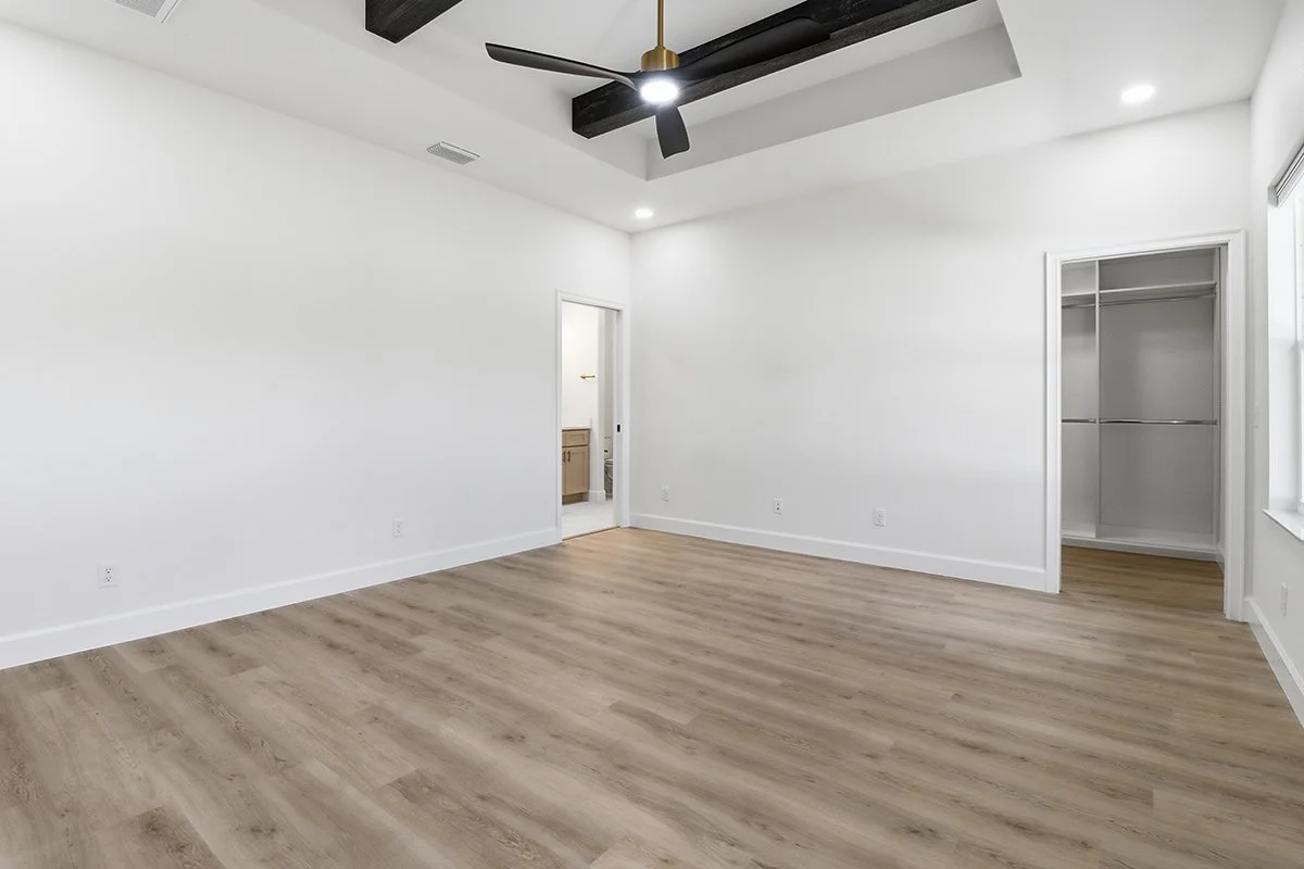 Empty room with white walls, wood flooring, ceiling fan, and built-in closet.