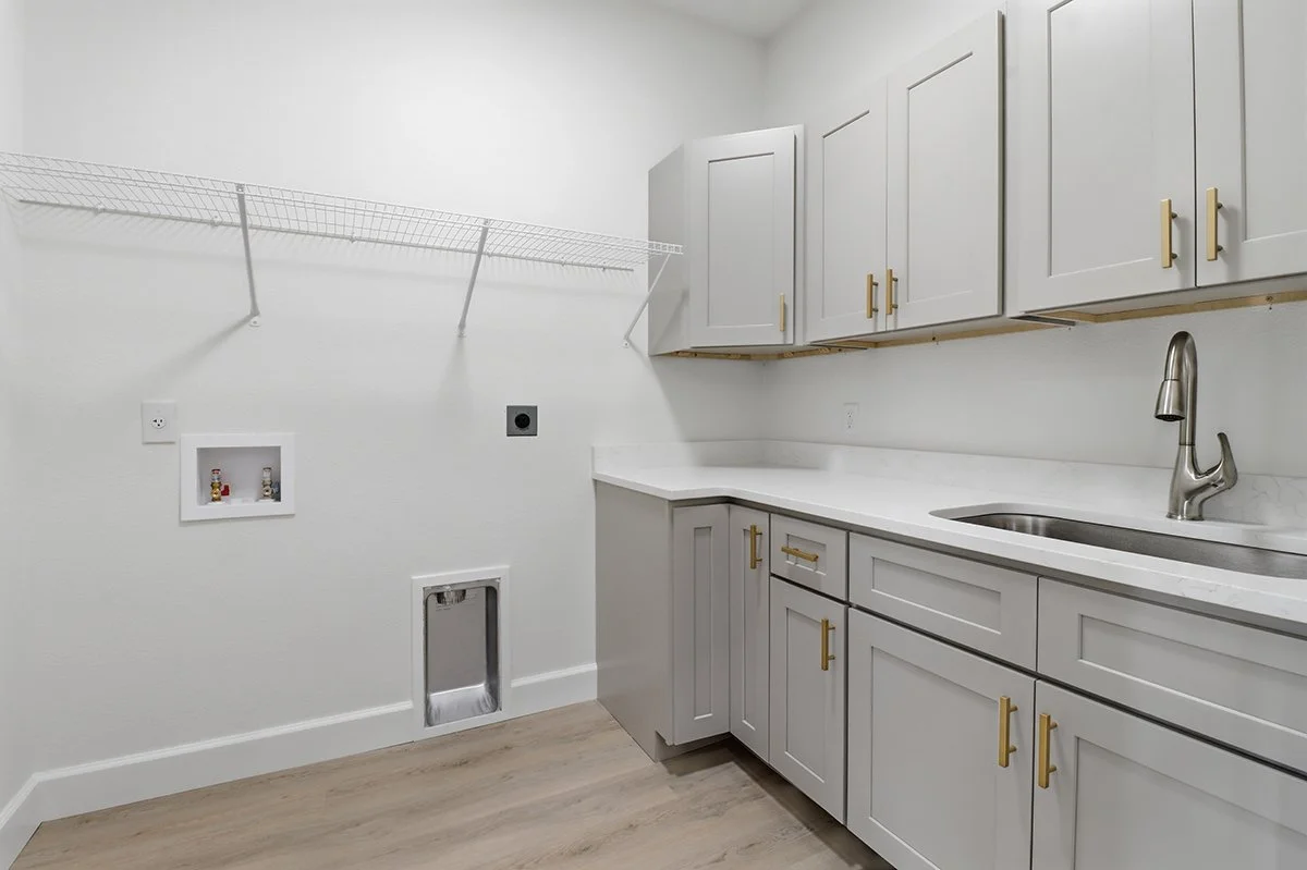 Empty laundry room with white cabinetry, a countertop, a sink, and a wire shelf. There are hookups for a washer and dryer along the wall.