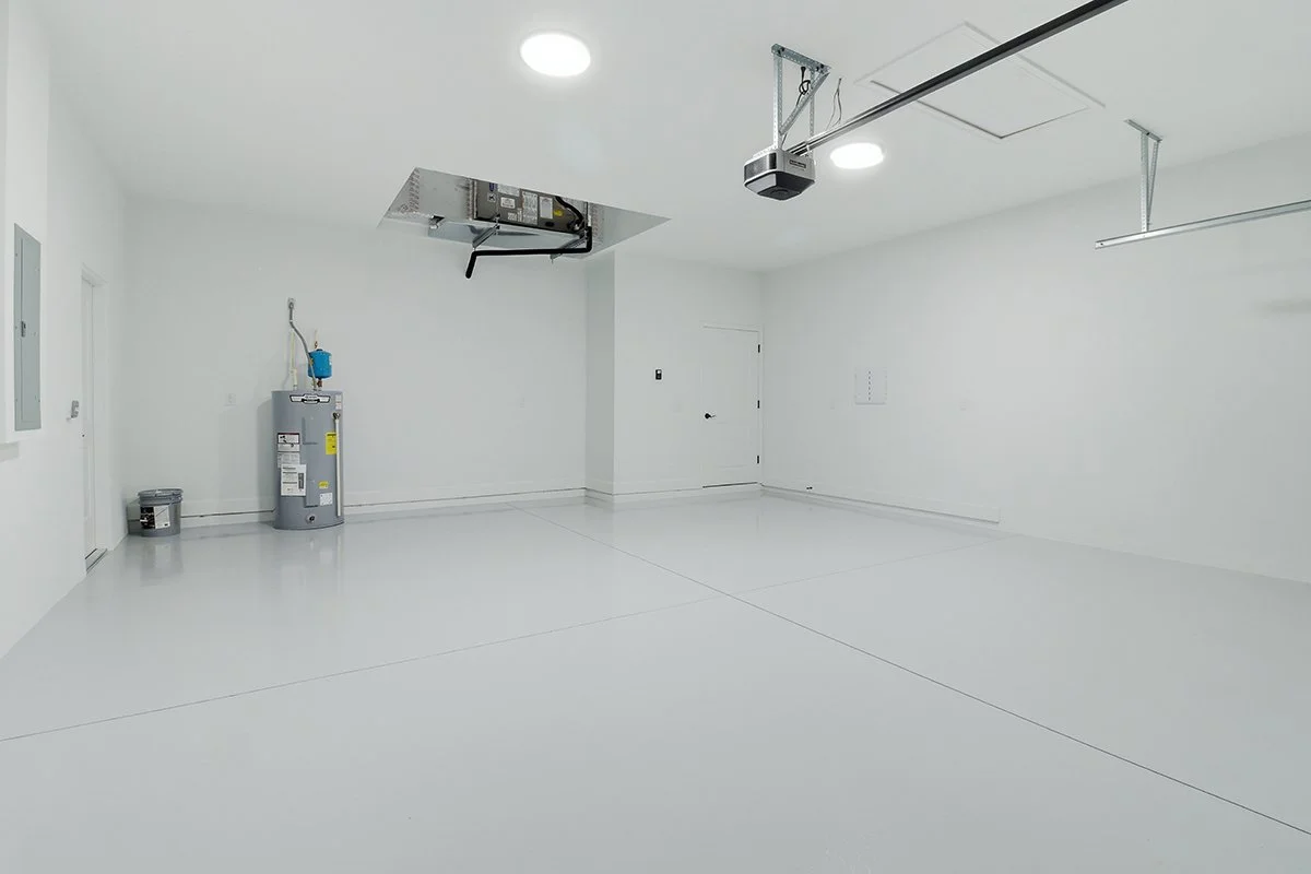 Empty garage with white walls and floor, water heater, electrical panel, and garage door opener ceiling system
