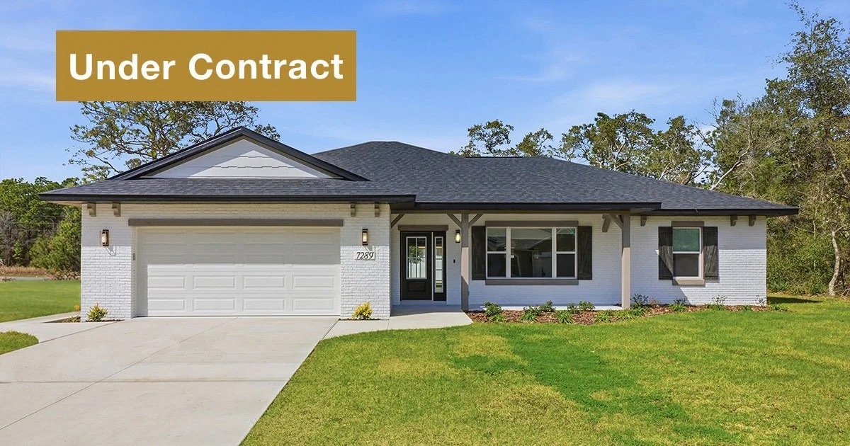Newly constructed Citrus Springs home with white painted brick exterior, a charcoal gray shingled roof, large front windows, a two car garage with white door. The homes has gray accents on the corbels and porch beams and a black front door