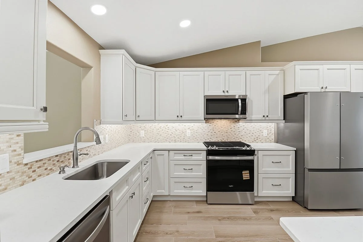 Modern kitchen with white cabinets, stainless steel appliances, a tile backsplash, and wood flooring.