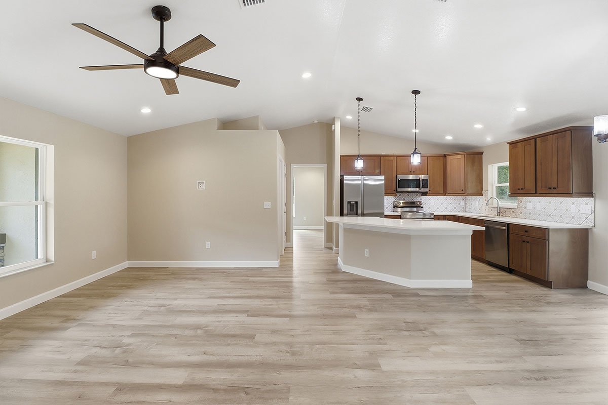 Open-concept kitchen and living area with wood flooring, beige walls, modern appliances, and a ceiling fan.