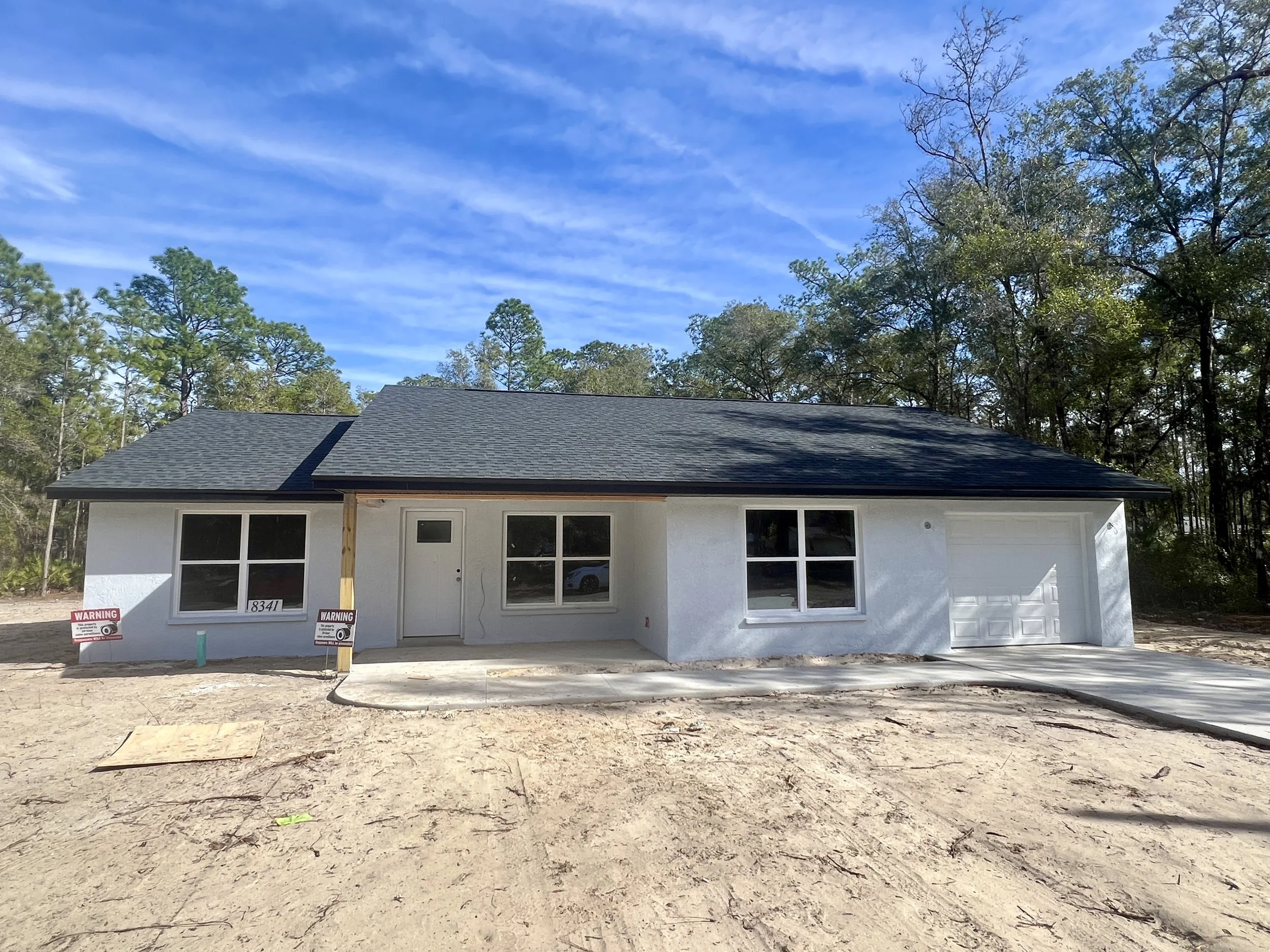 Newly constructed home with sage green stucco exterior, gray stone accents, covered front porch and two car garage