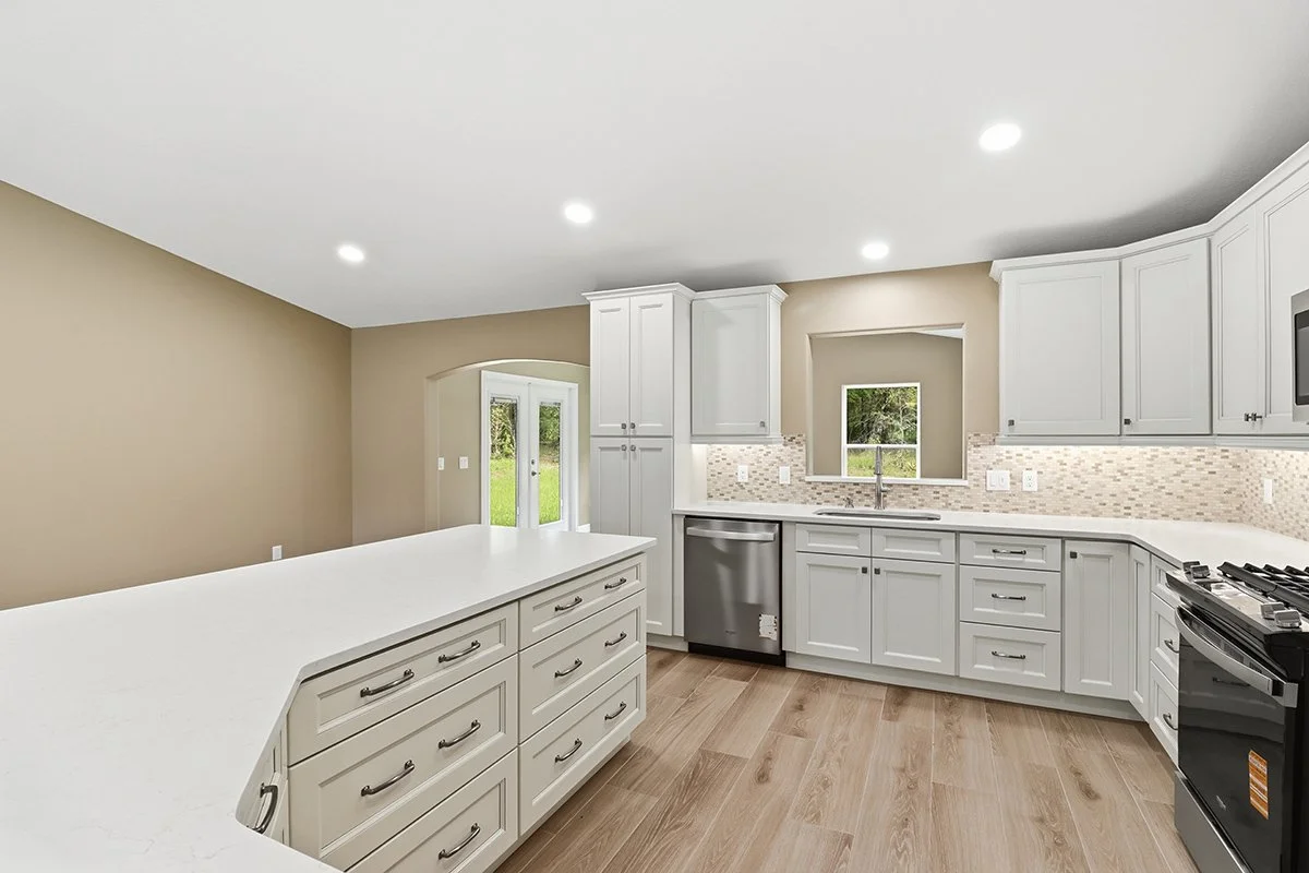 Modern kitchen with white cabinets, a central island, stainless steel appliances, light-colored tile backsplash, small window above the sink, hardwood floors, and beige walls.