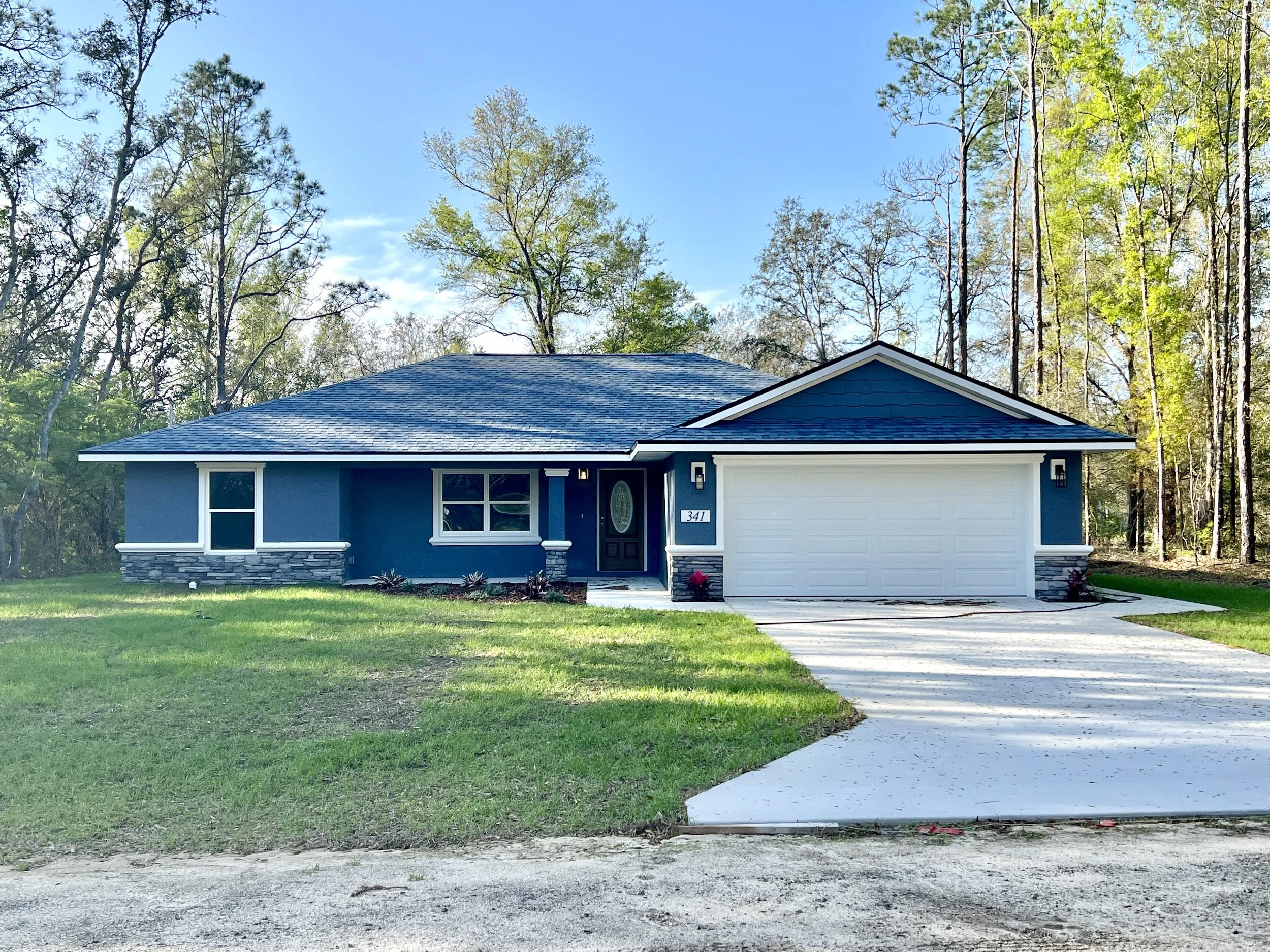 Single story newly constructed home painted deep blue with white accents and blue asphalt shingled roof on a grassy Citrus Springs lot with a concrete driveway and white 2-car garage door