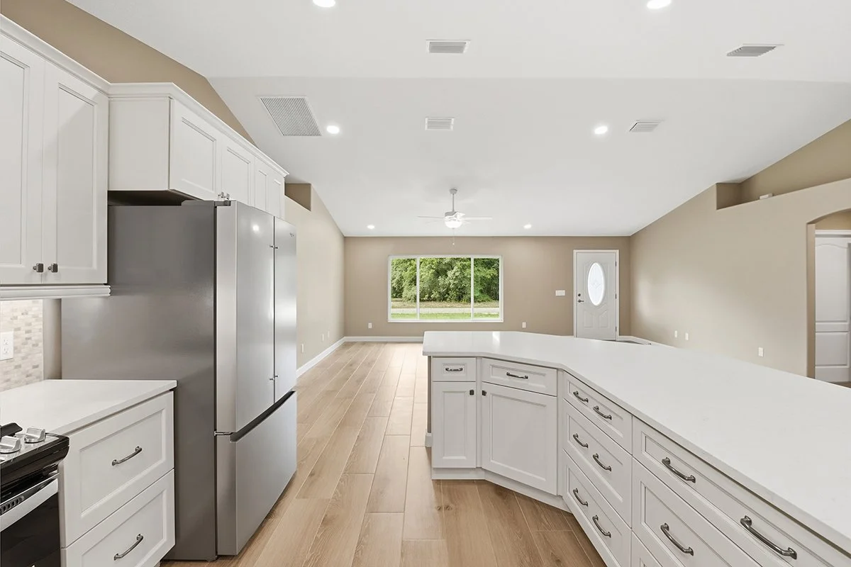 Open-concept kitchen with white cabinets, stainless steel refrigerator, and a large window in the living area with a view outside.