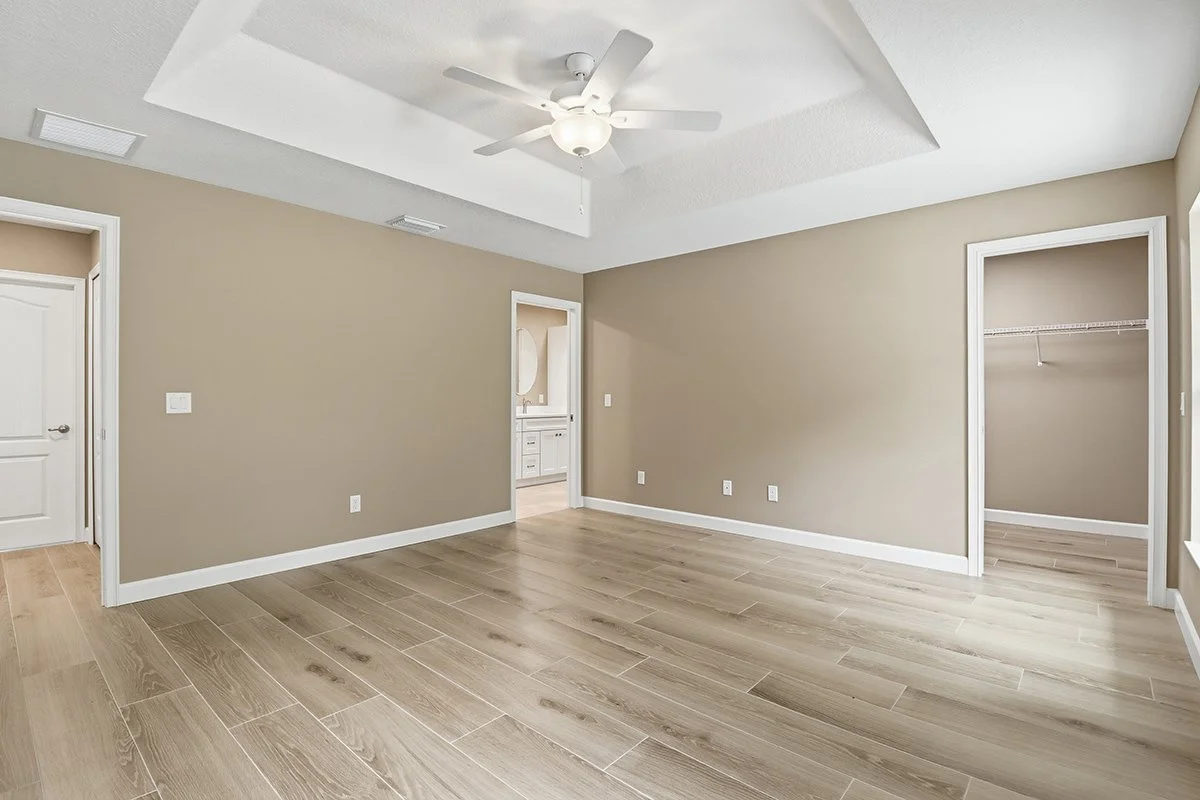 Empty beige room with wood flooring, beige walls, a ceiling fan, and two open closets.