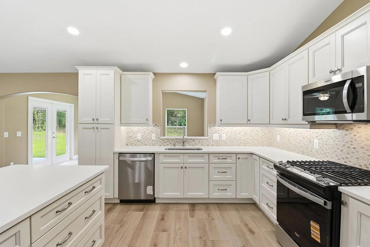 Modern kitchen with white cabinets, stainless steel appliances, a beige backsplash, and a light wood floor.