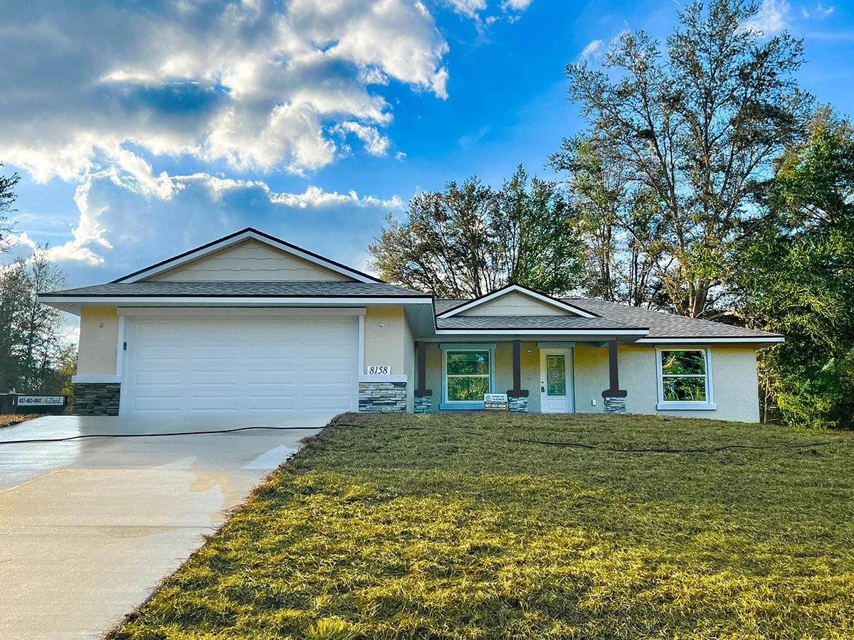 Concrete block home under construction that hasn't been painted but has a vaulted roof, 2 car garage and stonework on the lower half of the front of the home