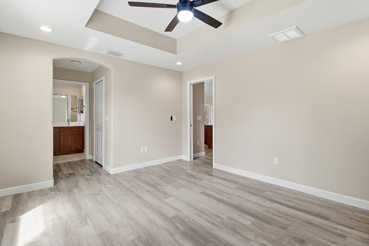 Empty room with beige walls, light wood flooring, ceiling fan, recessed lighting, and two doorways leading to other rooms.