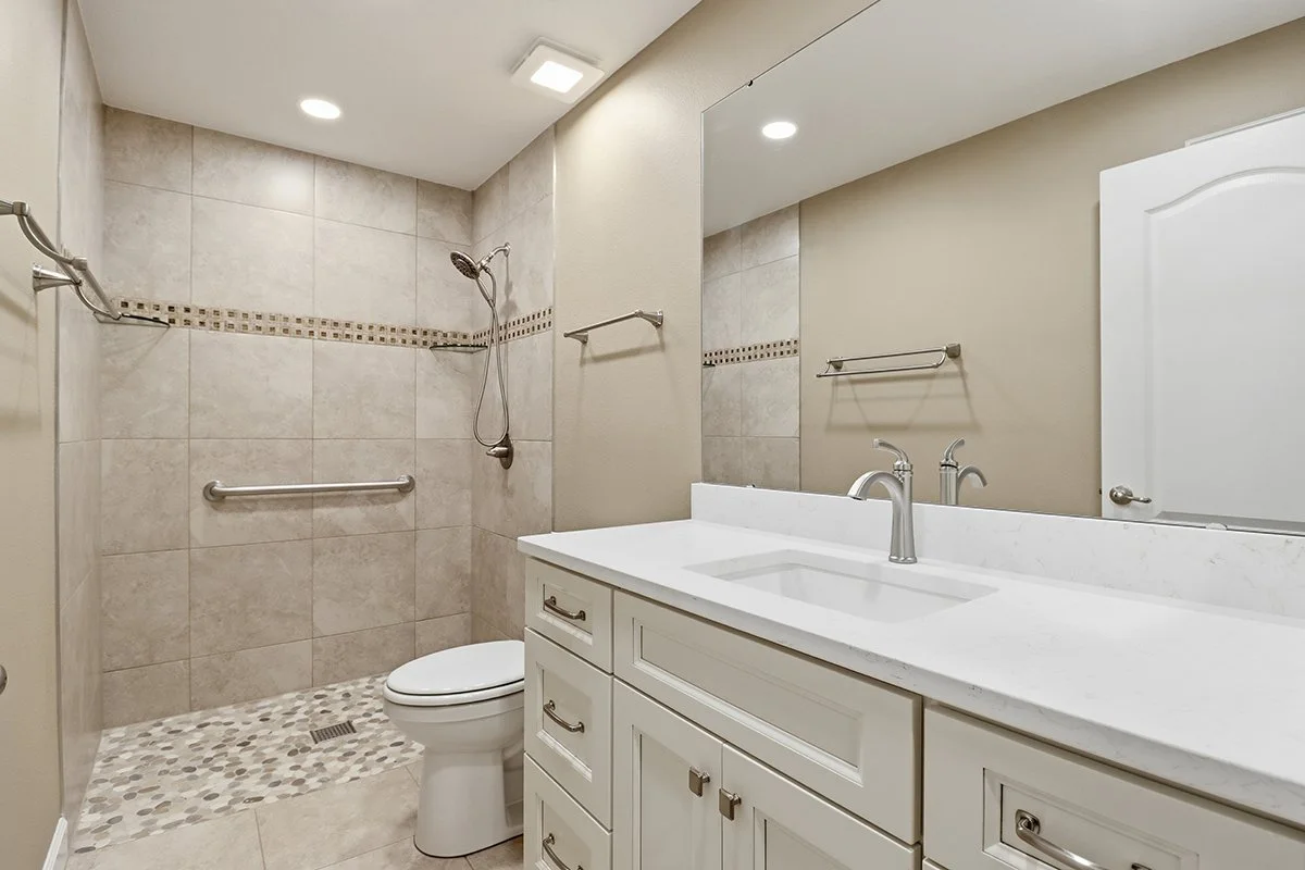 Bathroom with walk-in shower, toilet, and white vanity with sink, large mirror, beige walls, and tile decor