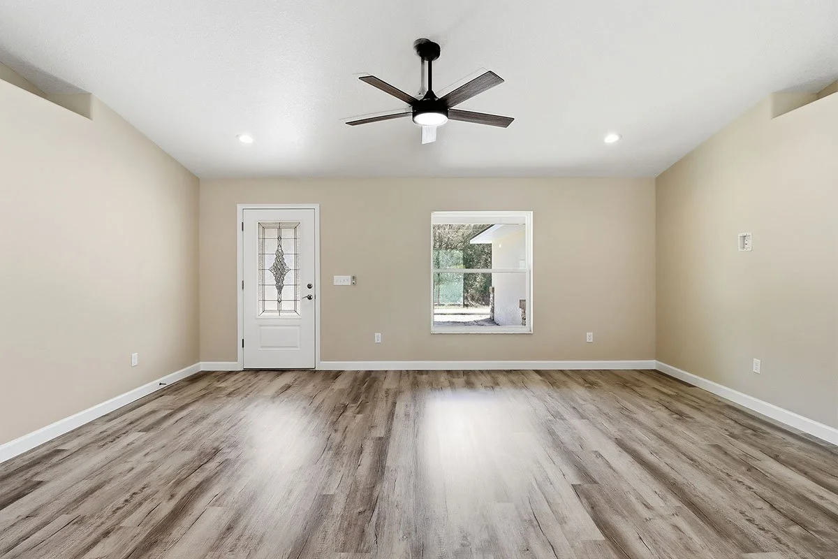 Empty living room with beige walls, hardwood flooring, a ceiling fan, window, and door with decorative glass.