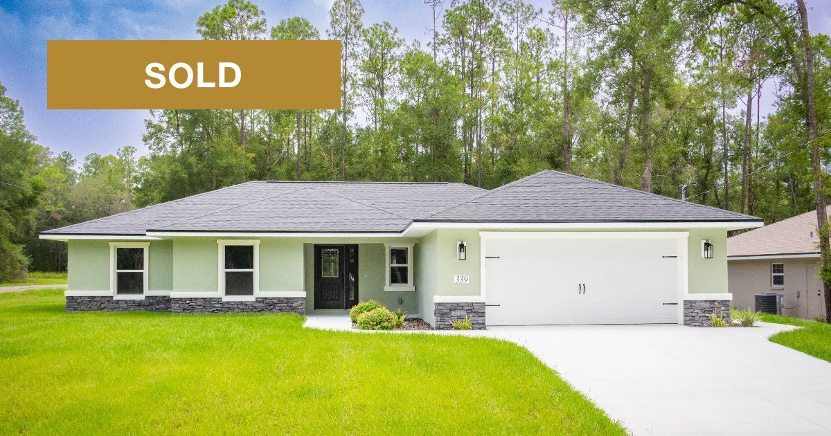 Newly constructed home with light green stucco exterior, gray stone accents, covered front porch and two car garage