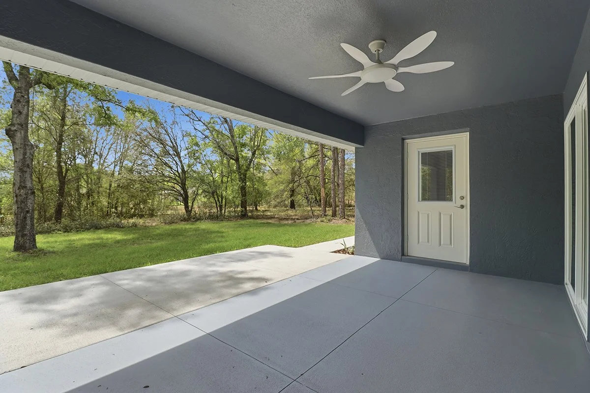 Covered porch with a ceiling fan, a door, and a view of green grass and trees outside.