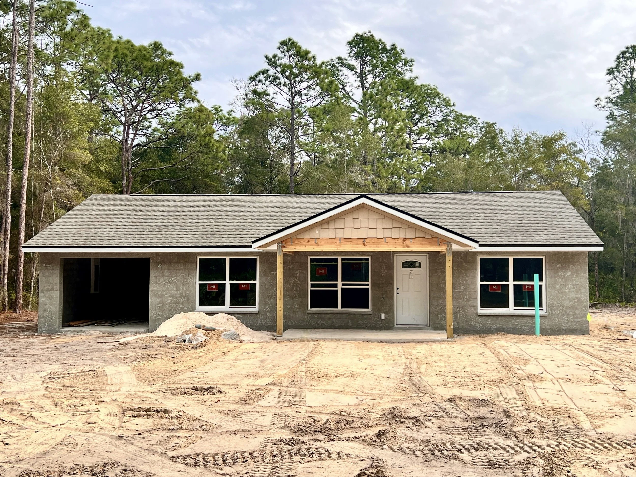 Exterior of an unpainted single story home currently under construction with grey asphalt shingled roof and sitting on a dirt lot without grass yet