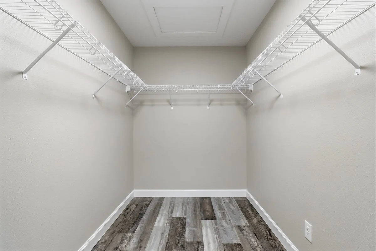 Empty walk-in closet with white wire shelving on both sides, wood-look flooring, and an accessible ceiling vent.