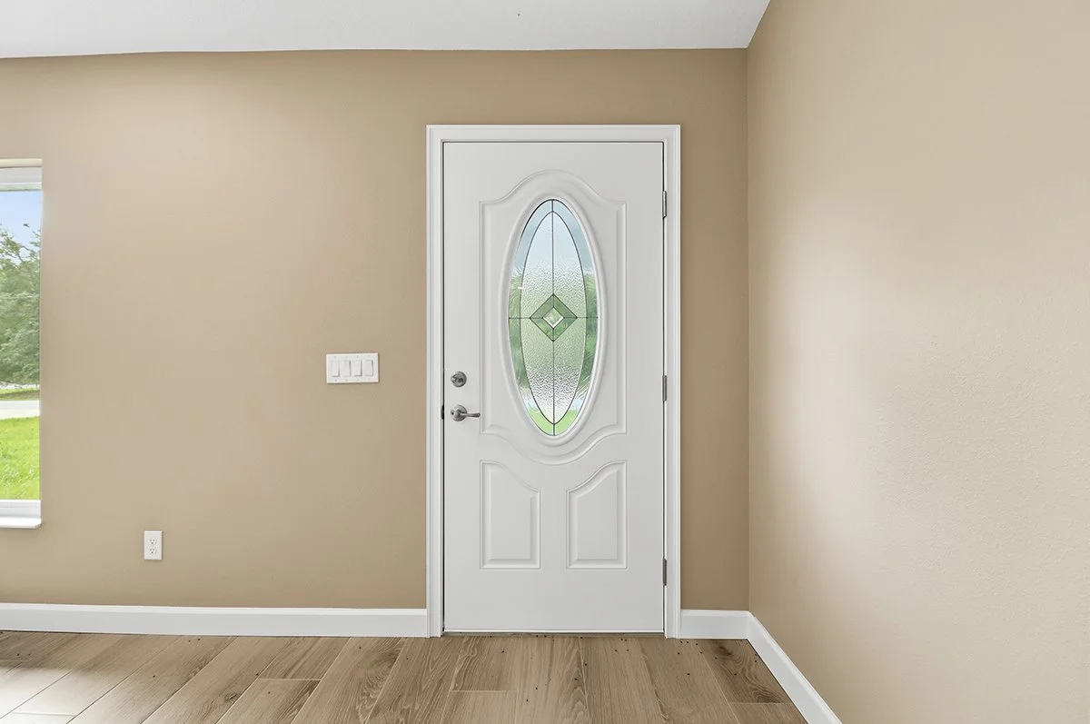 White front door with decorative glass panel in a beige room with wooden flooring.