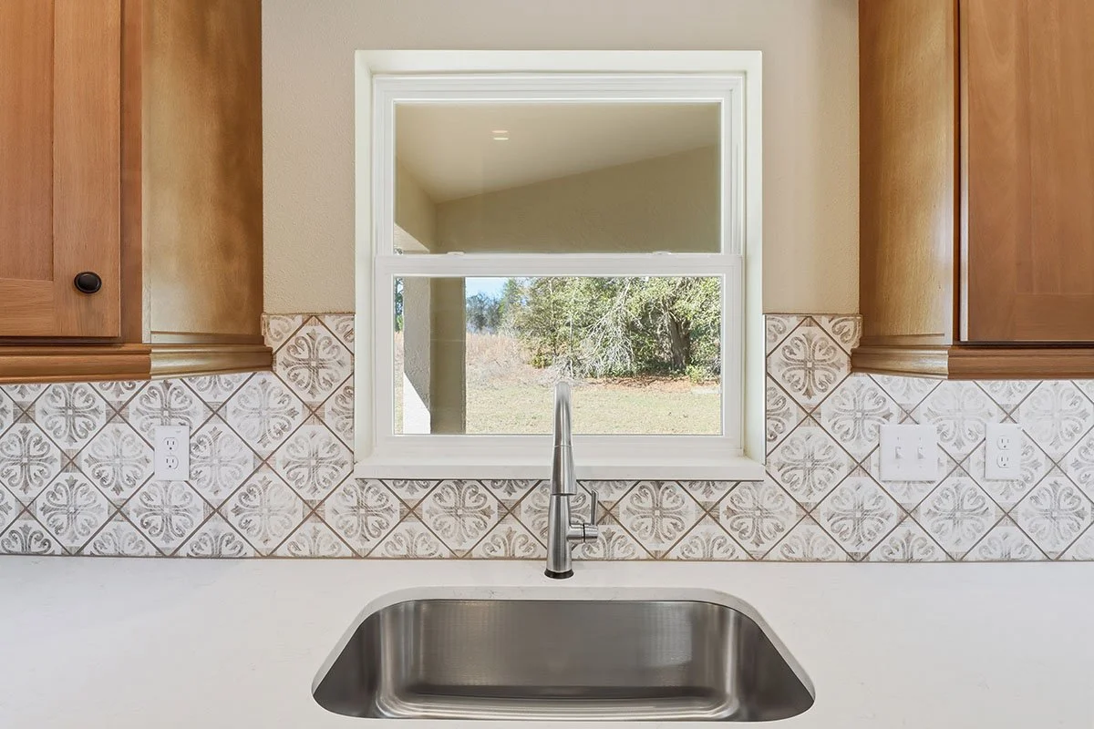 Kitchen sink beneath a double-pane window with a view of a backyard and trees.