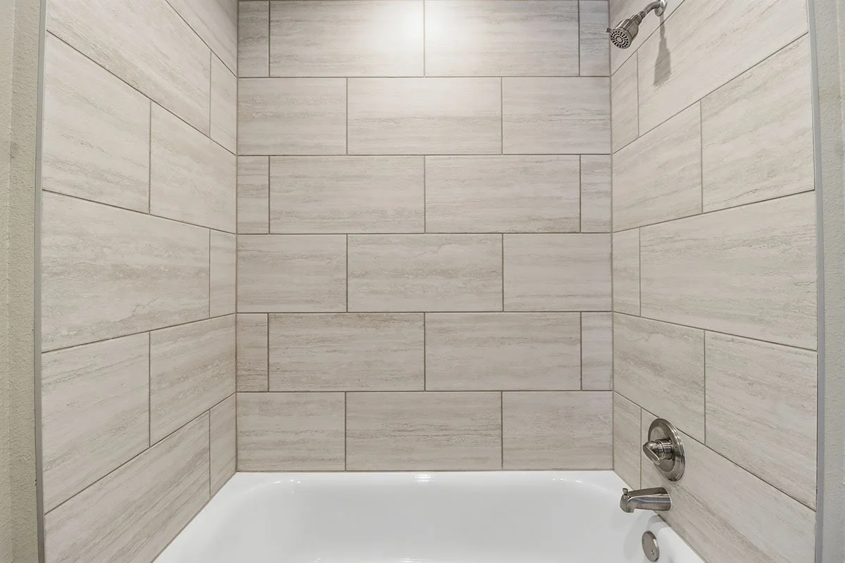 Empty tiled shower with a showerhead and a faucet on the right wall.