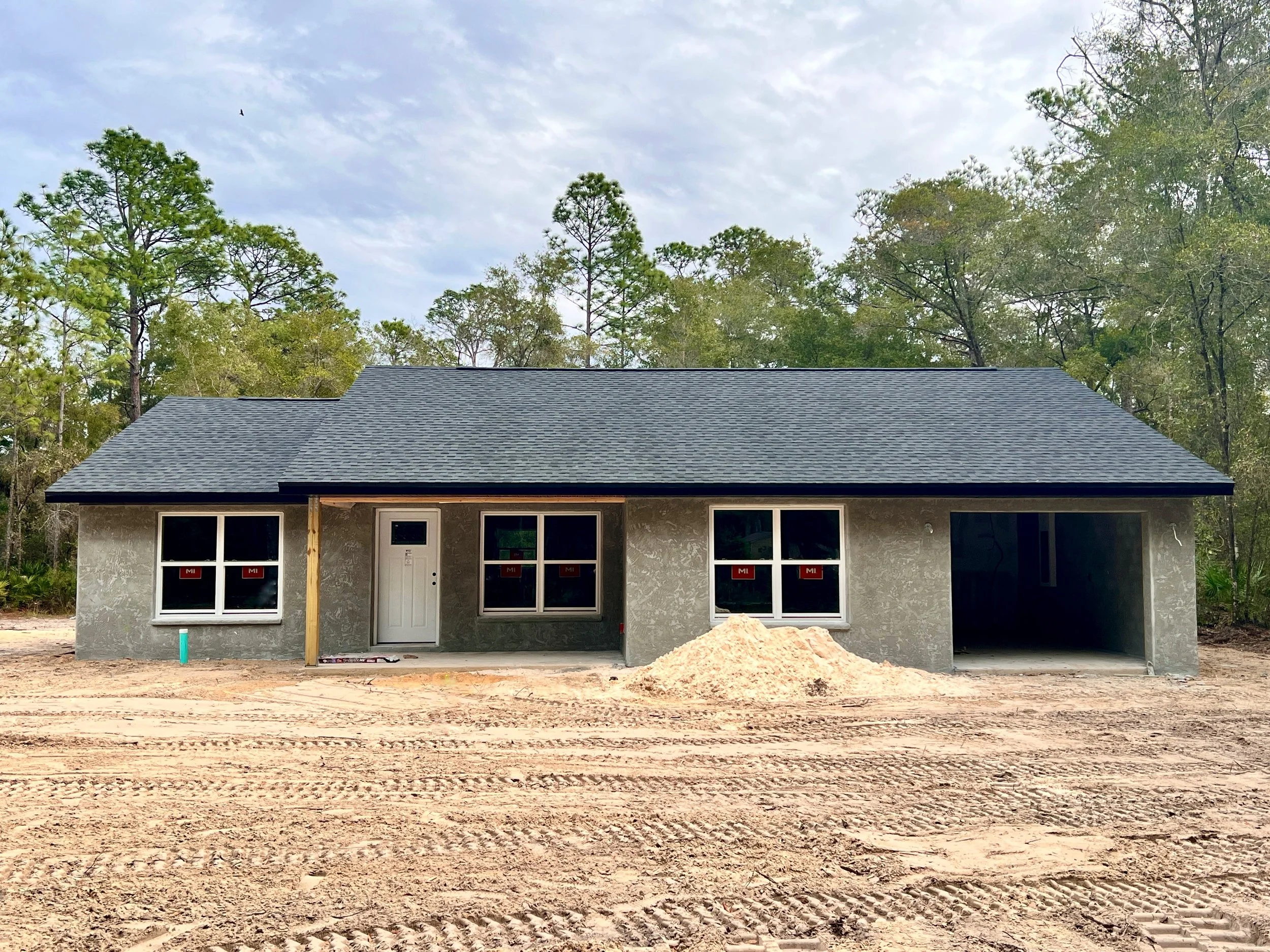 Newly constructed home with sage green stucco exterior, gray stone accents, covered front porch and two car garage