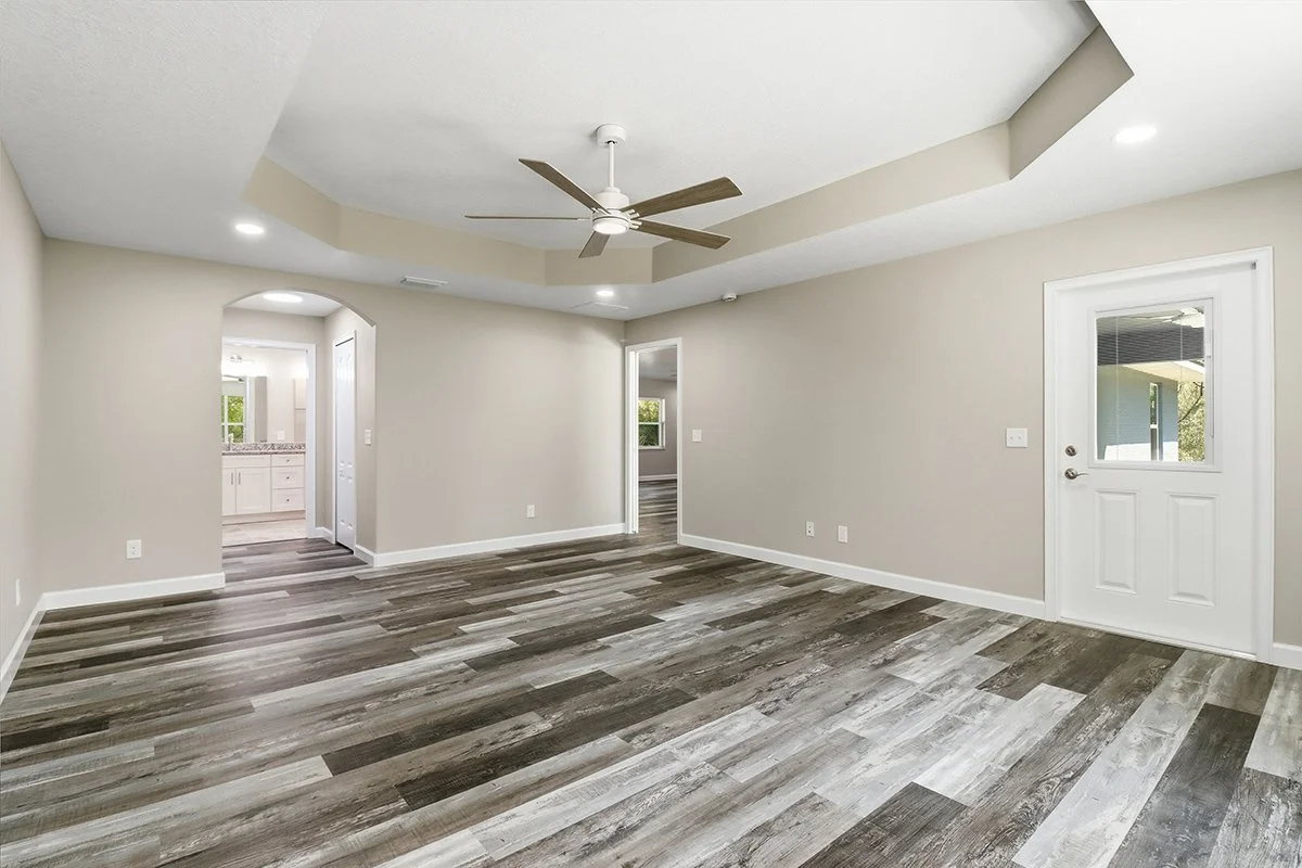 Empty living room with wood flooring, ceiling fan, and recessed lighting, leading to a kitchen and additional rooms.