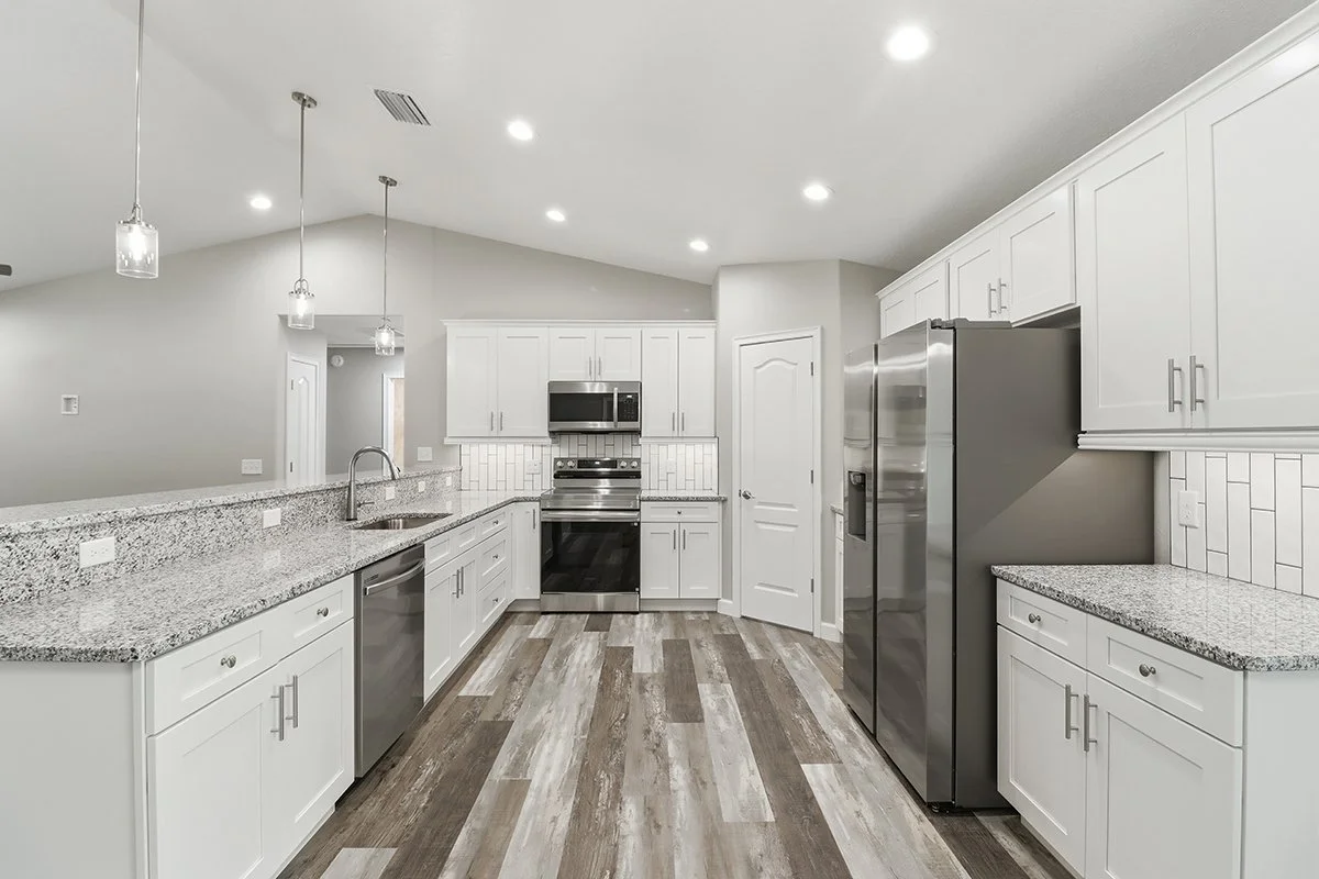 Modern kitchen with white cabinets, stainless steel appliances, granite countertops, and wood-look flooring.