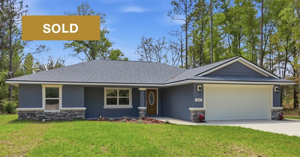 Single story newly constructed home painted deep blue with white accents and blue asphalt shingled roof on a grassy Citrus Springs lot with a concrete driveway and white 2-car garage door