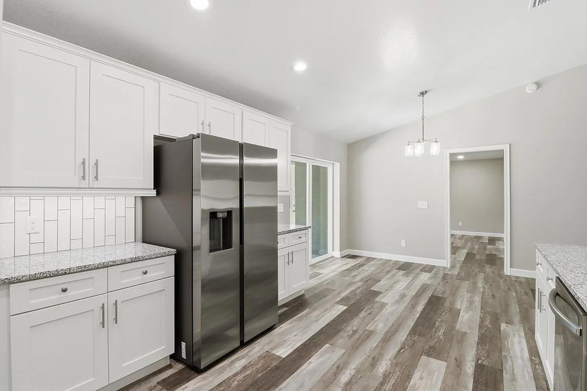Modern kitchen with white cabinets, granite countertops, stainless steel refrigerator, and wood-look flooring.