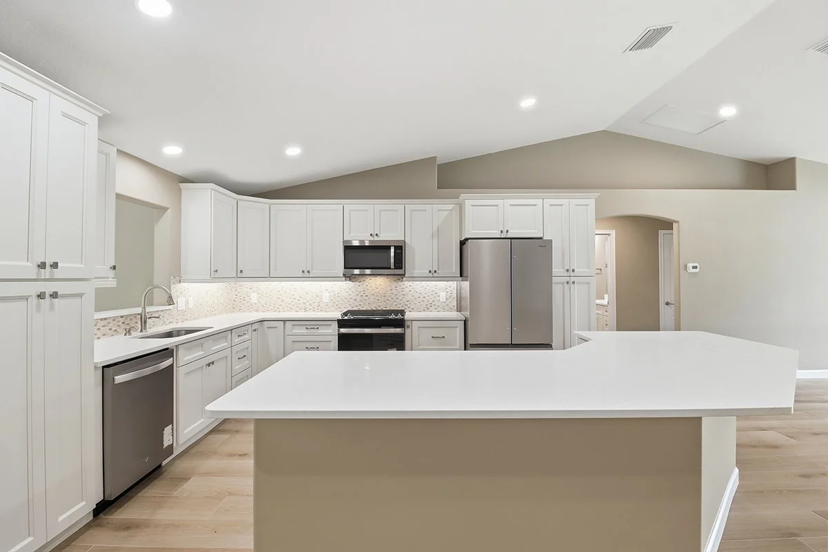 Modern kitchen with white cabinets, stainless steel appliances, beige walls, wood flooring, and an island counter.