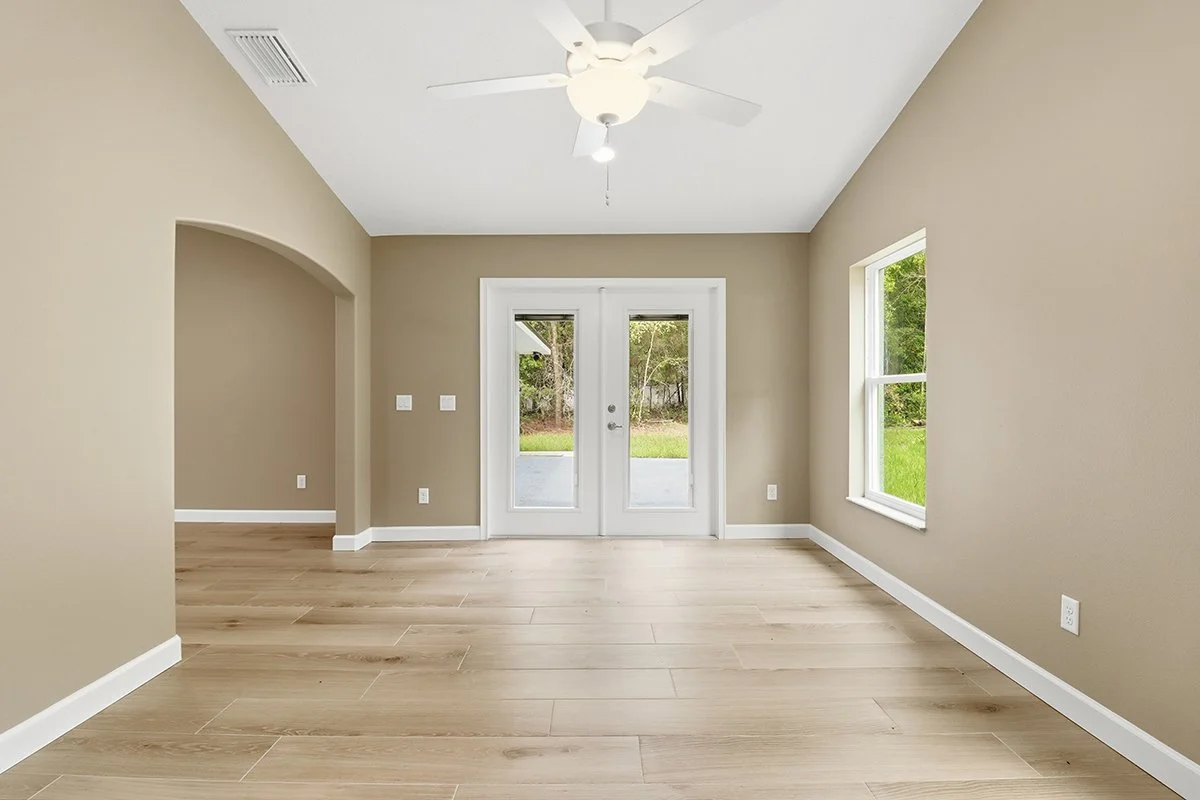 Empty living room with beige walls, wood flooring, a ceiling fan, and double glass doors leading outside.