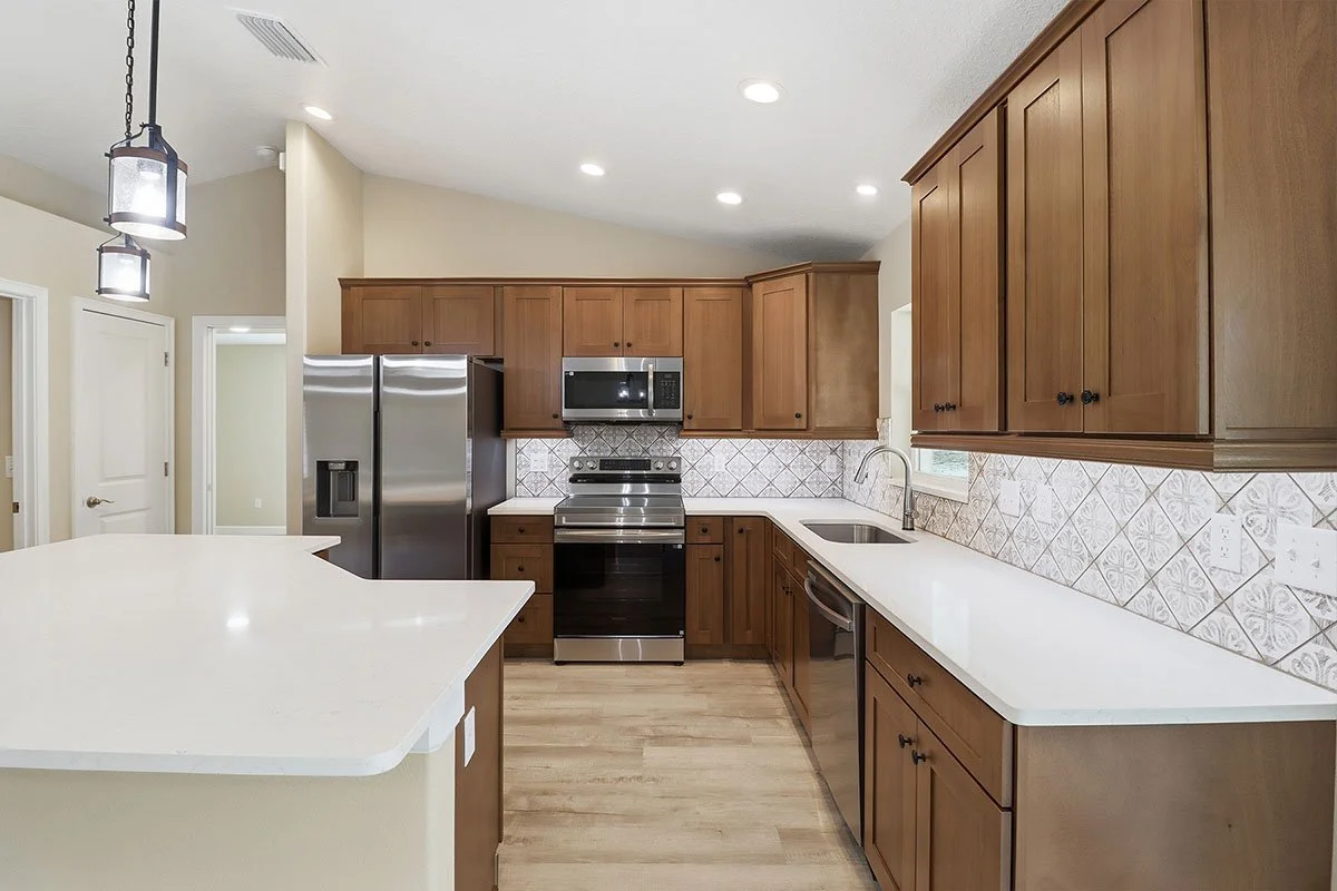 Kitchen with wooden cabinets, stainless steel appliances, white countertop, tiled backsplash, and hardwood floor.