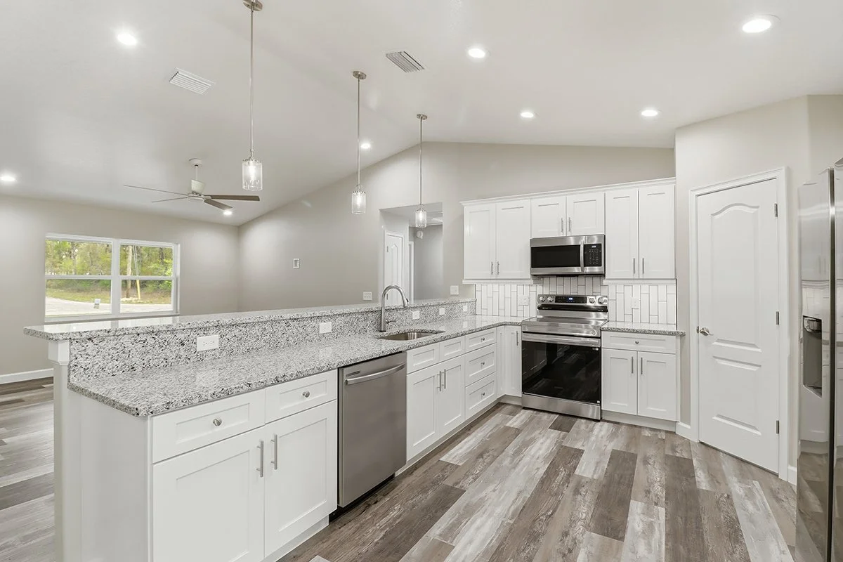 Modern kitchen with white cabinets, stainless steel appliances, granite countertops, and wood-look flooring.
