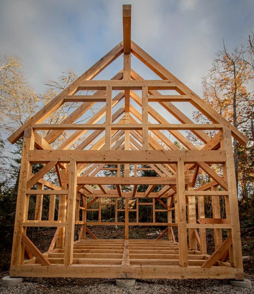 Unfinished wooden timber frame structure in forest setting.