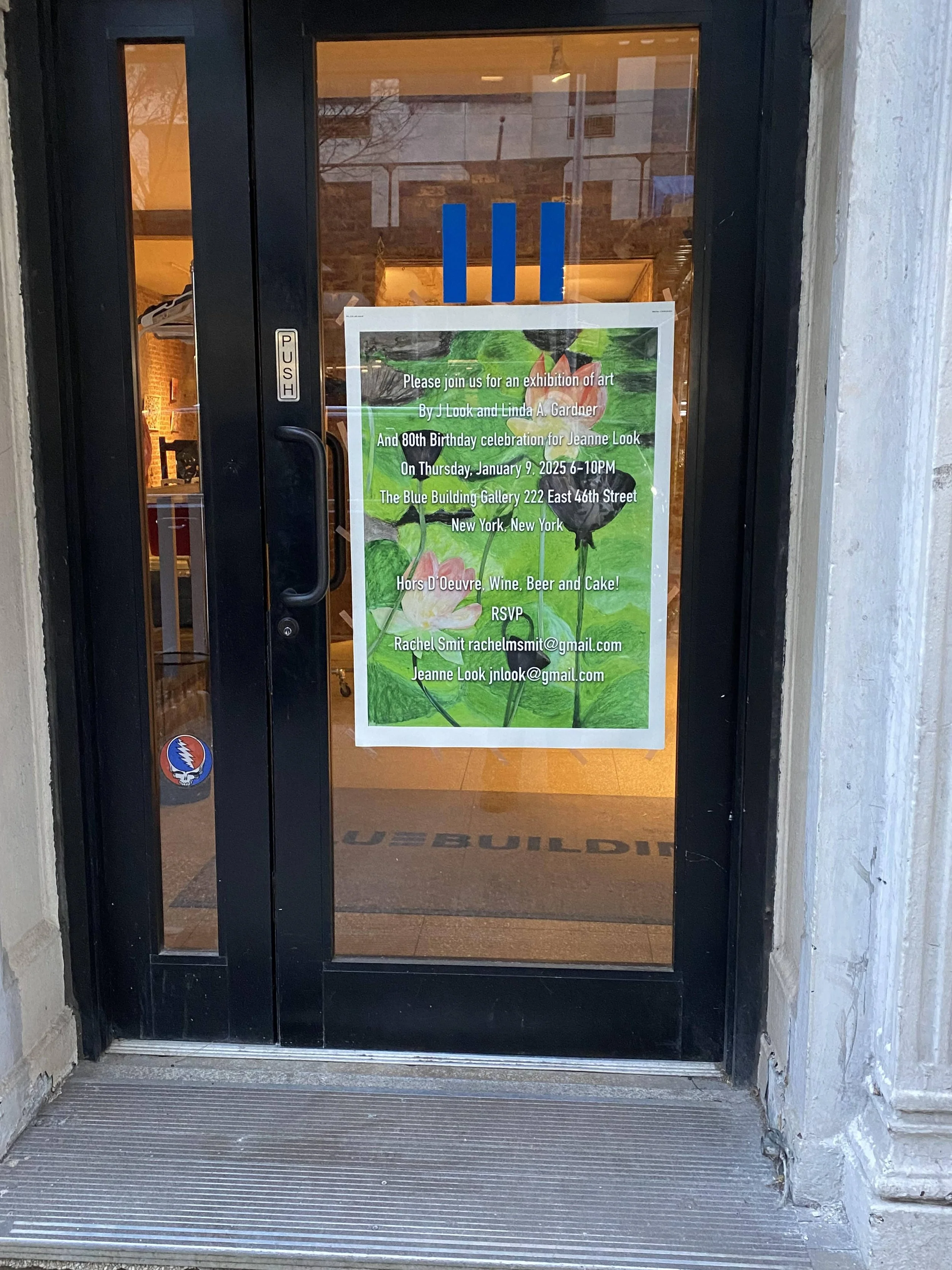 A door with a poster announcing an art exhibition and birthday celebration inside, with a reflective glass surface showing the street outside.