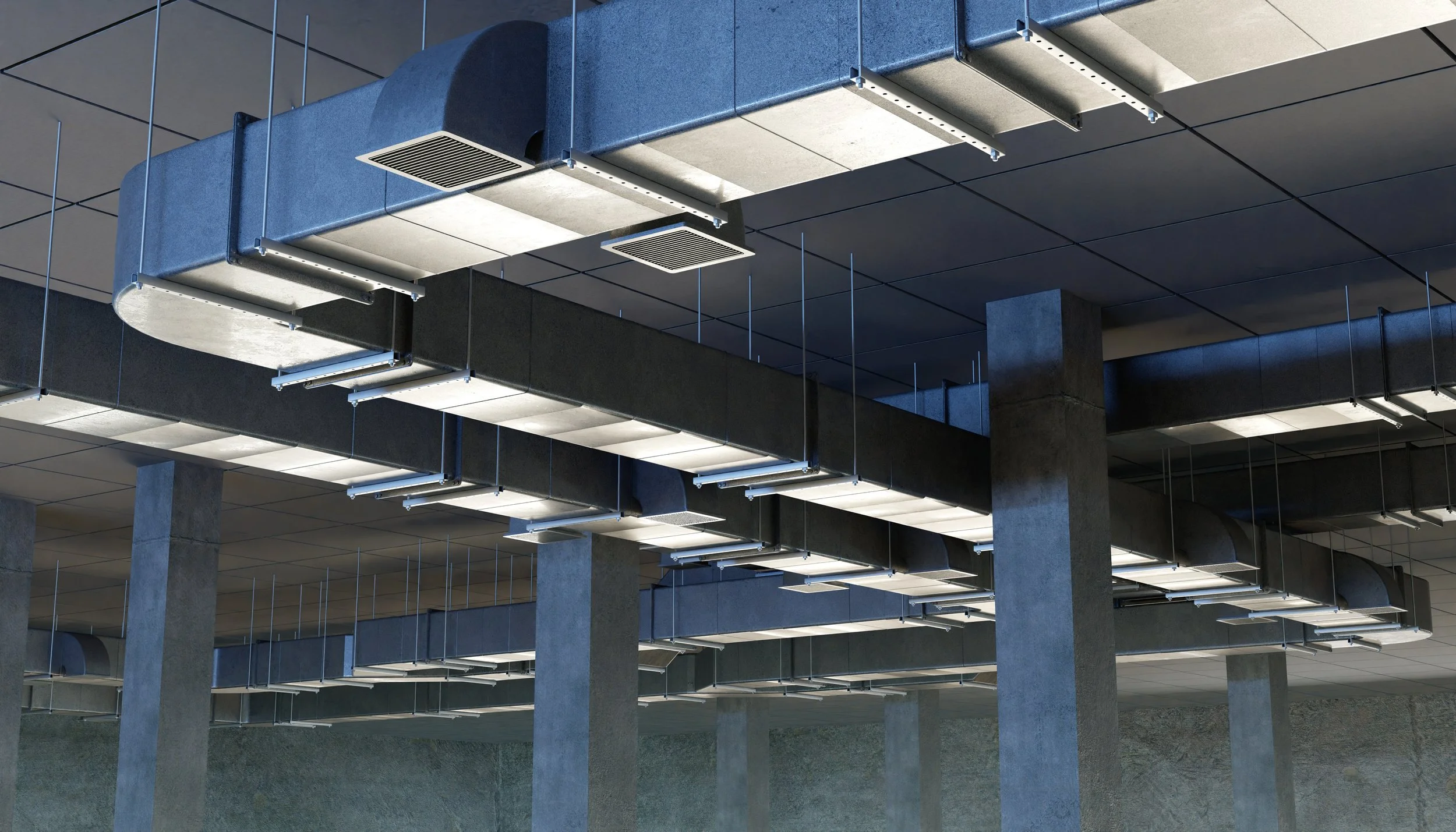 Interior view of a modern building with exposed HVAC ducts and ceiling tiles, supported by concrete pillars.