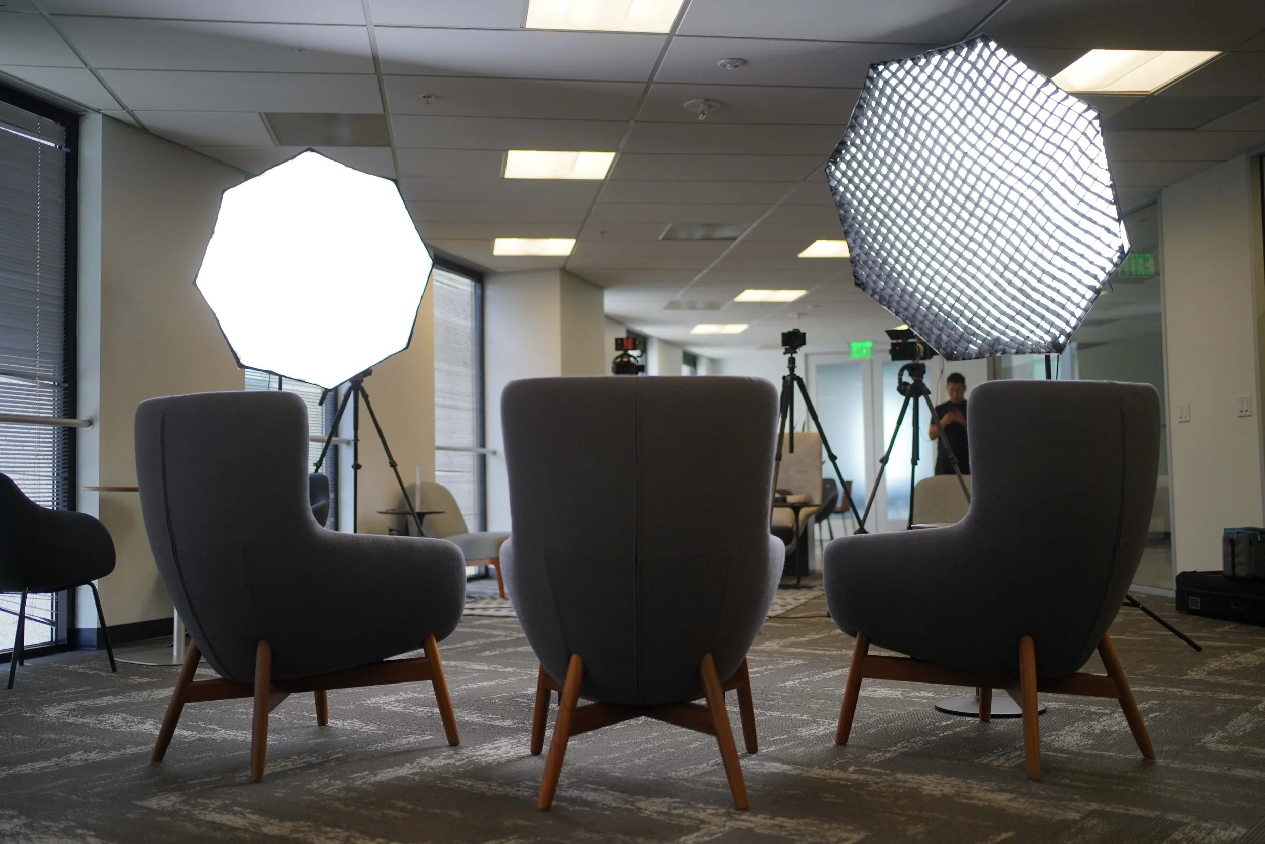 2 soft boxes with lights behind 3 chairs. A testimonial video recording setup.