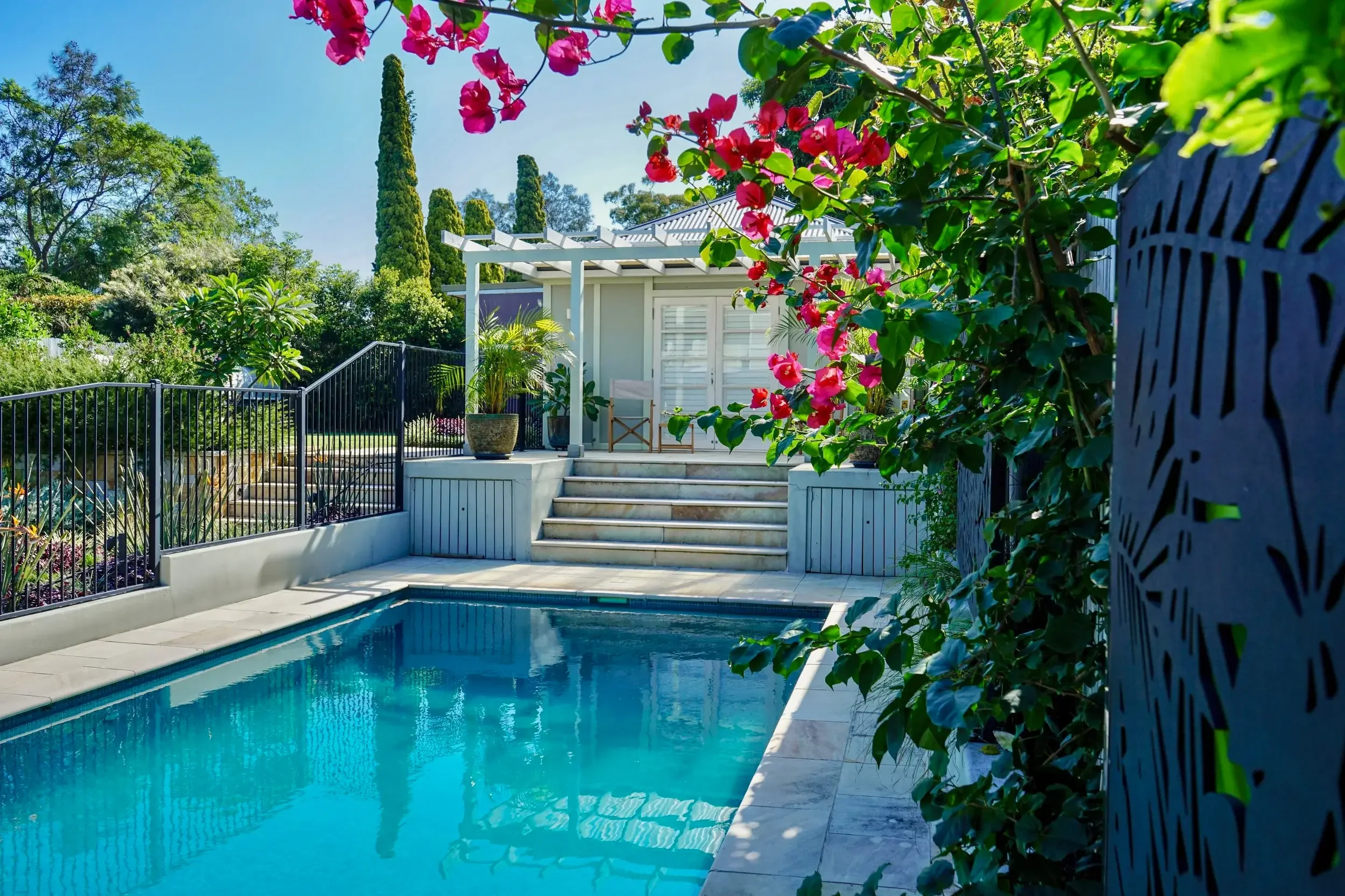 Stone patio with outdoor seating and lush garden planting around it with a pool